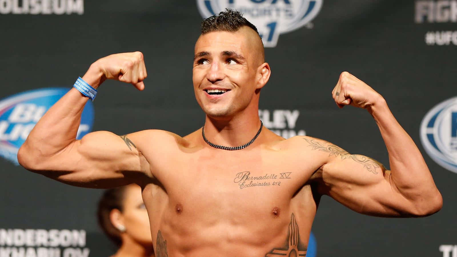 MMA 桌布 壁紙 — 一位赤裸上身的肌肉發達拳手在UFC稱重活動中自信微笑並彎曲雙臂。