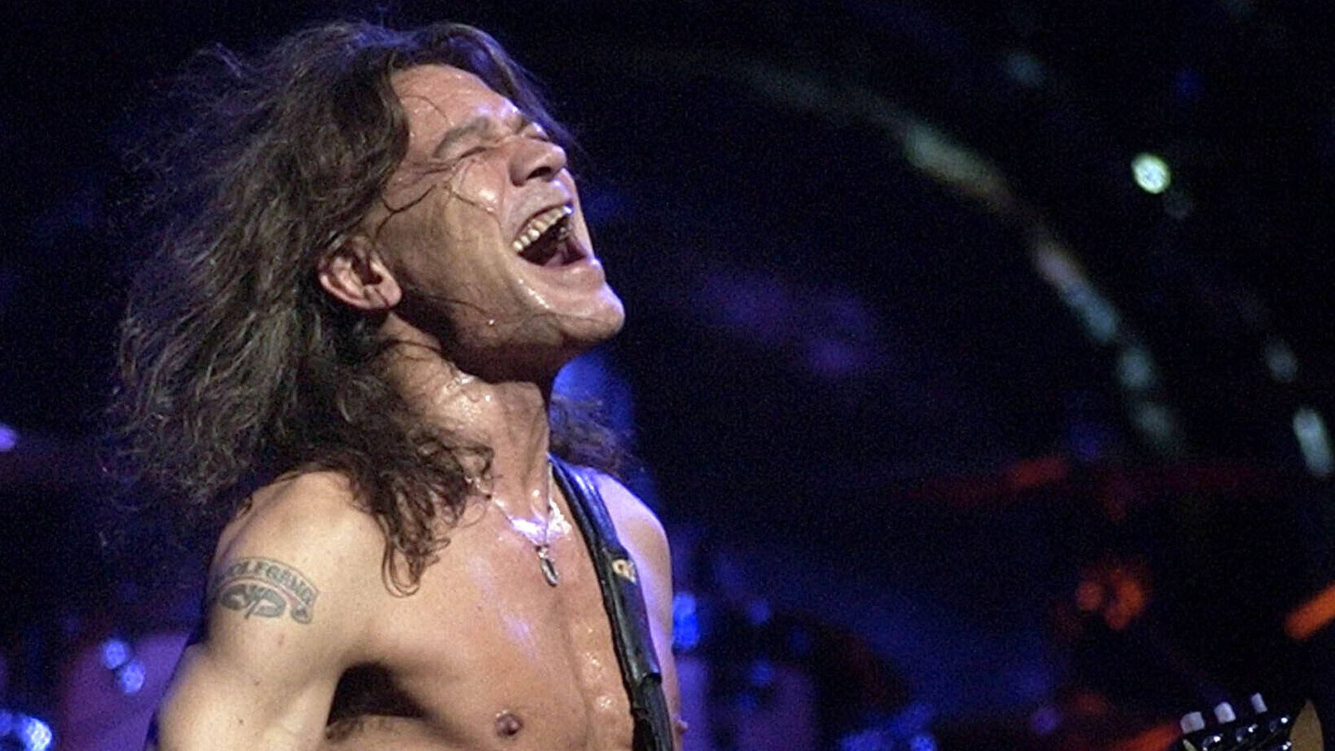 Eddie 桌布 壁紙 — 一位赤裸上身的長髮搖滾吉他手在現場演唱會中，在舞台燈光下激情吶喊。
