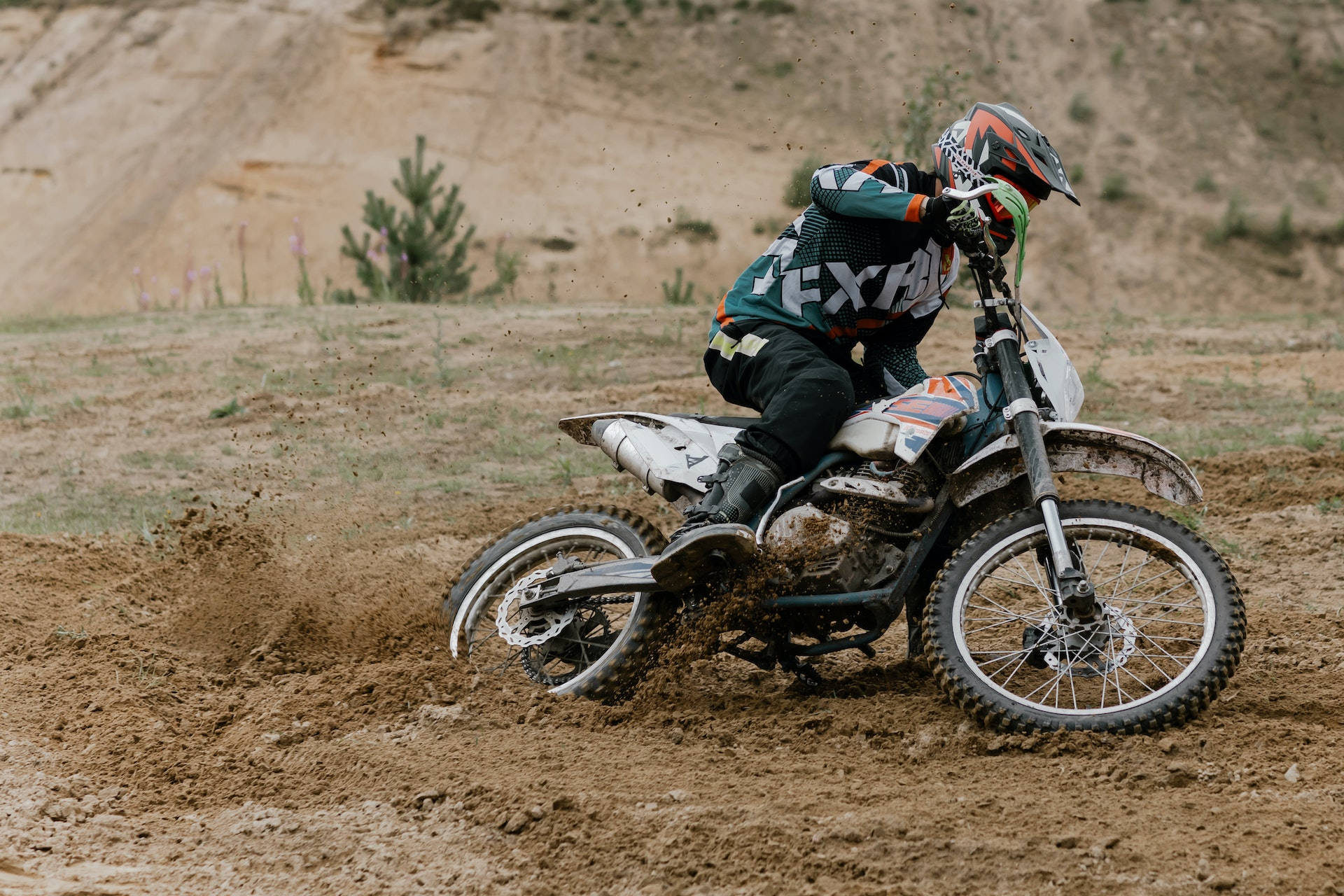 Motocross 桌布 壁紙 — 一位越野摩托車手在乾燥草地上騎著越野摩托車轉彎時濺起泥漿。