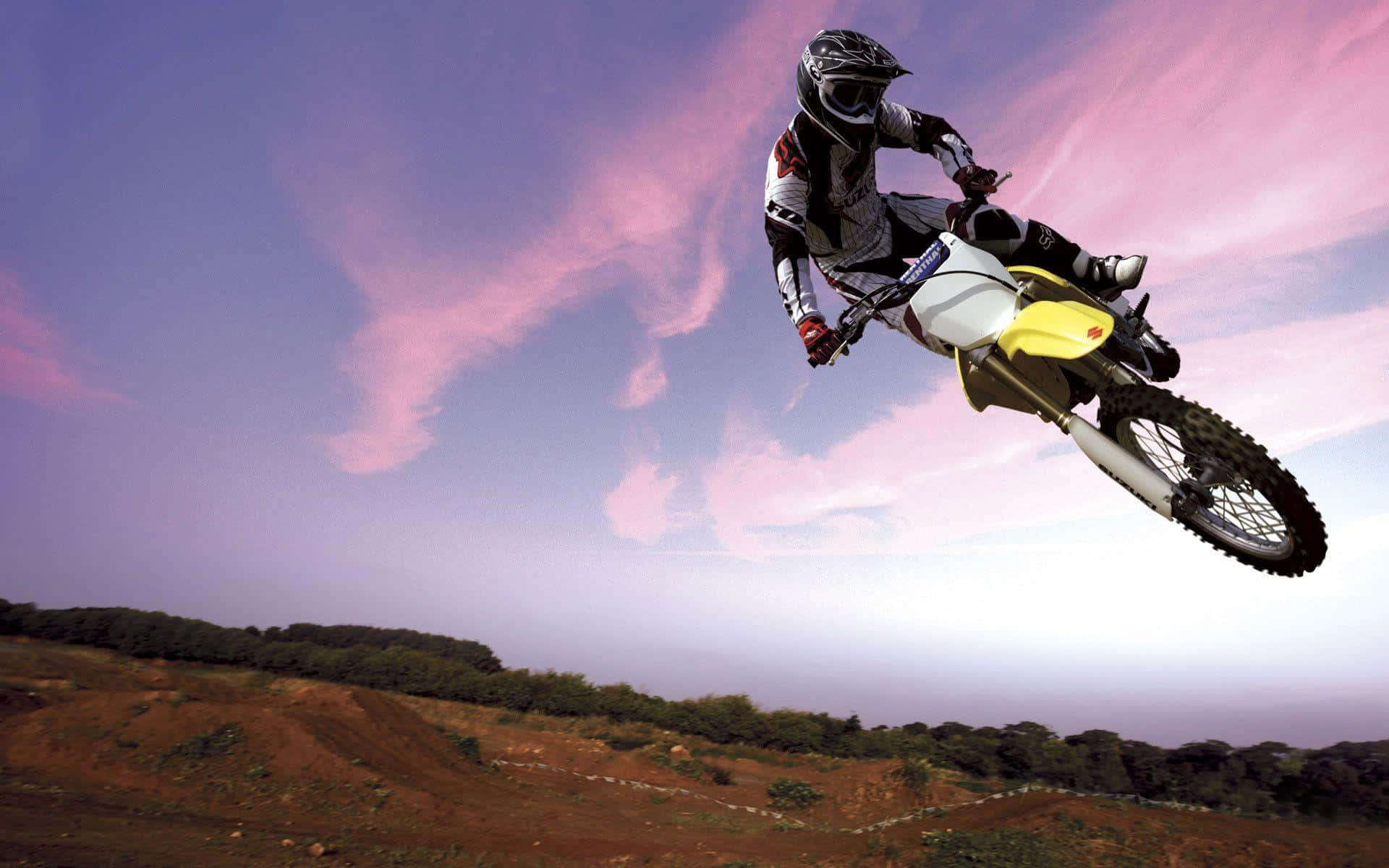 Motocross 桌布 壁紙 — 一位越野摩托車手在崎嶇的泥地上方，飛越充滿活力的粉紅與紫色暮色天空。