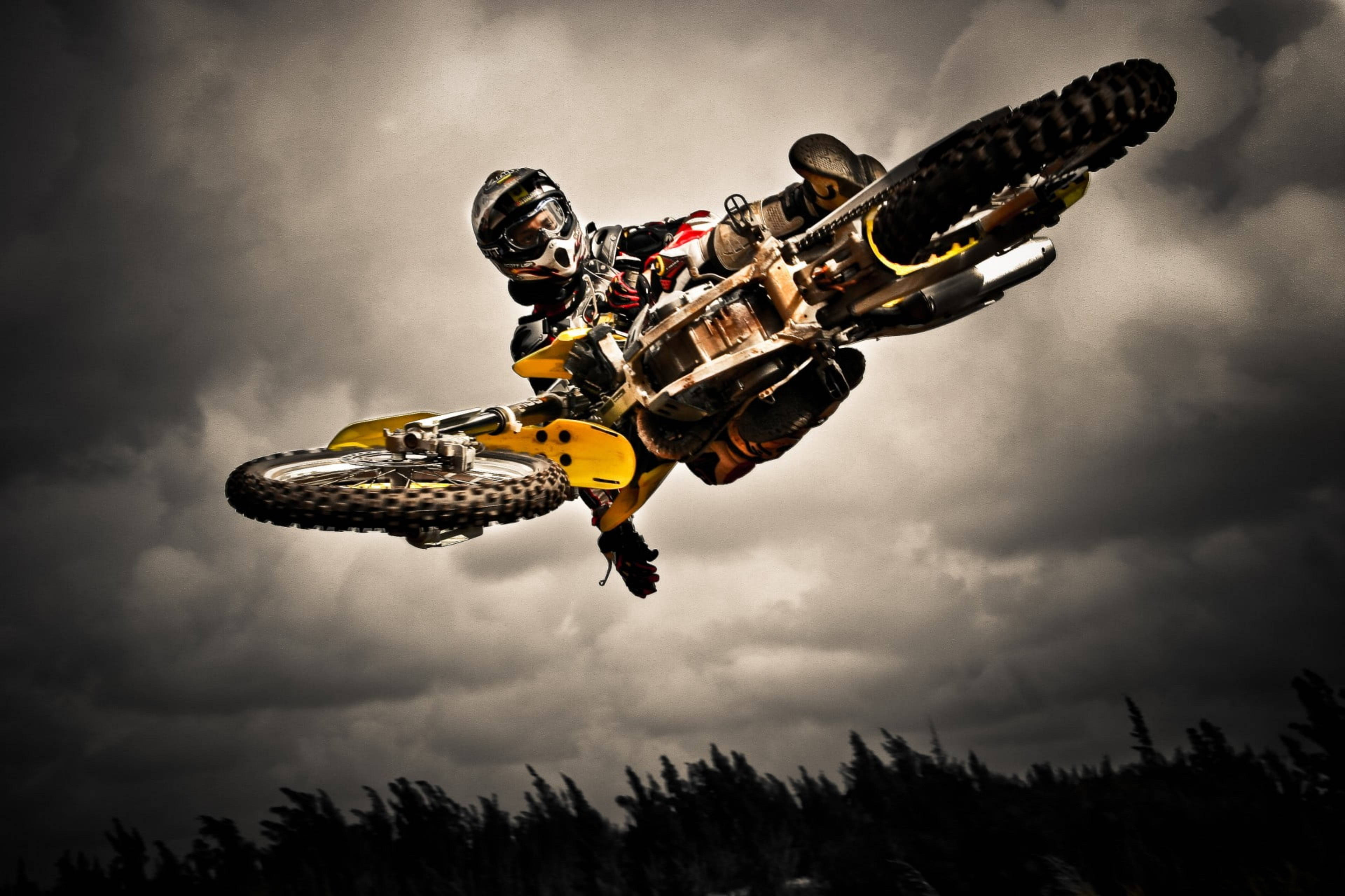 Extreme Sports 桌布 壁紙 — 一位越野摩托車手在暴風雨的天空下騎著黃色摩托車飛翔，表演極限空中特技。