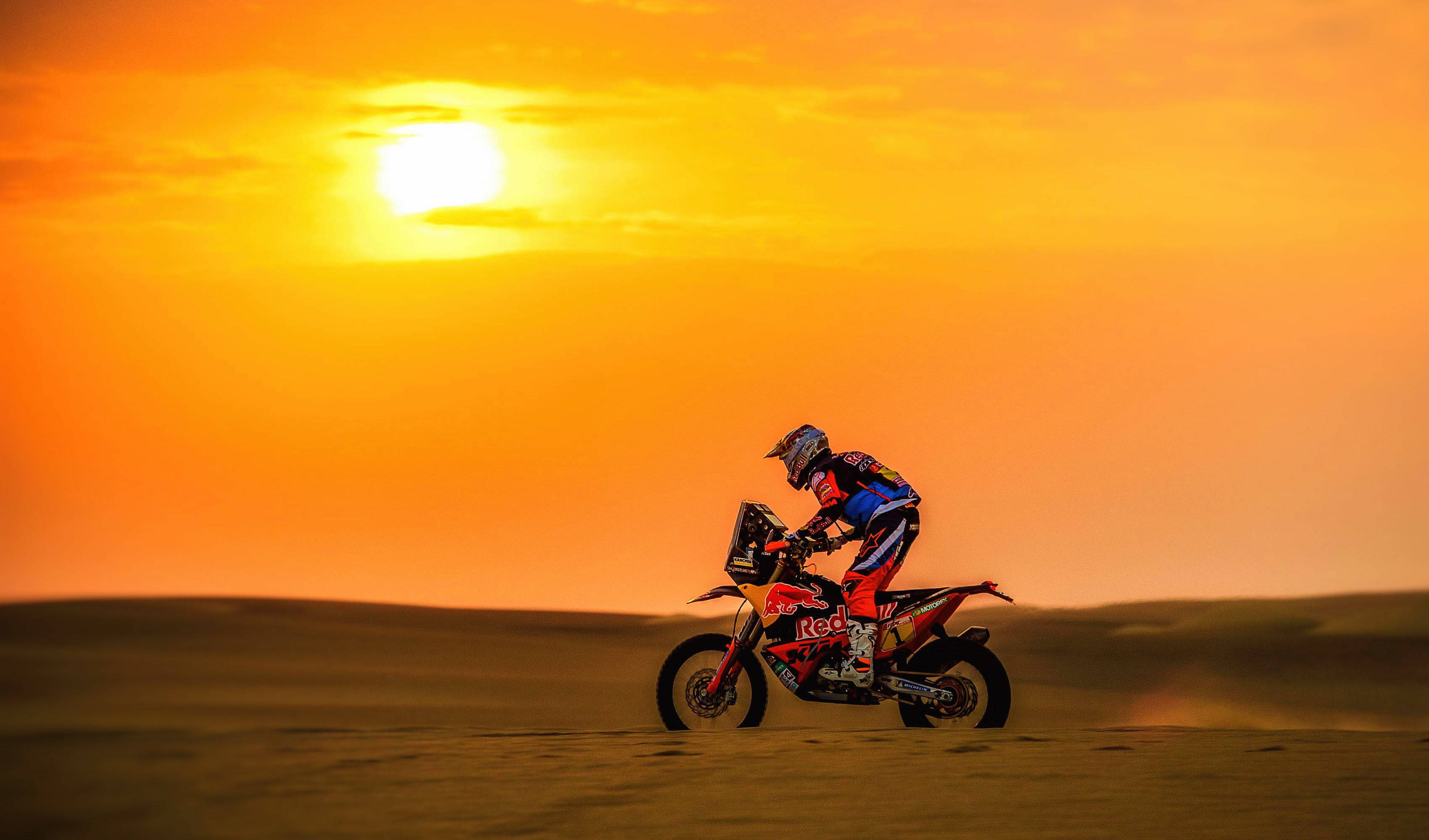KTM 摩托車 桌布 壁紙 — 一位越野摩托車手在沙漠沙丘上傾斜入彎，夕陽以火熱的橙色和黃色色調落下。