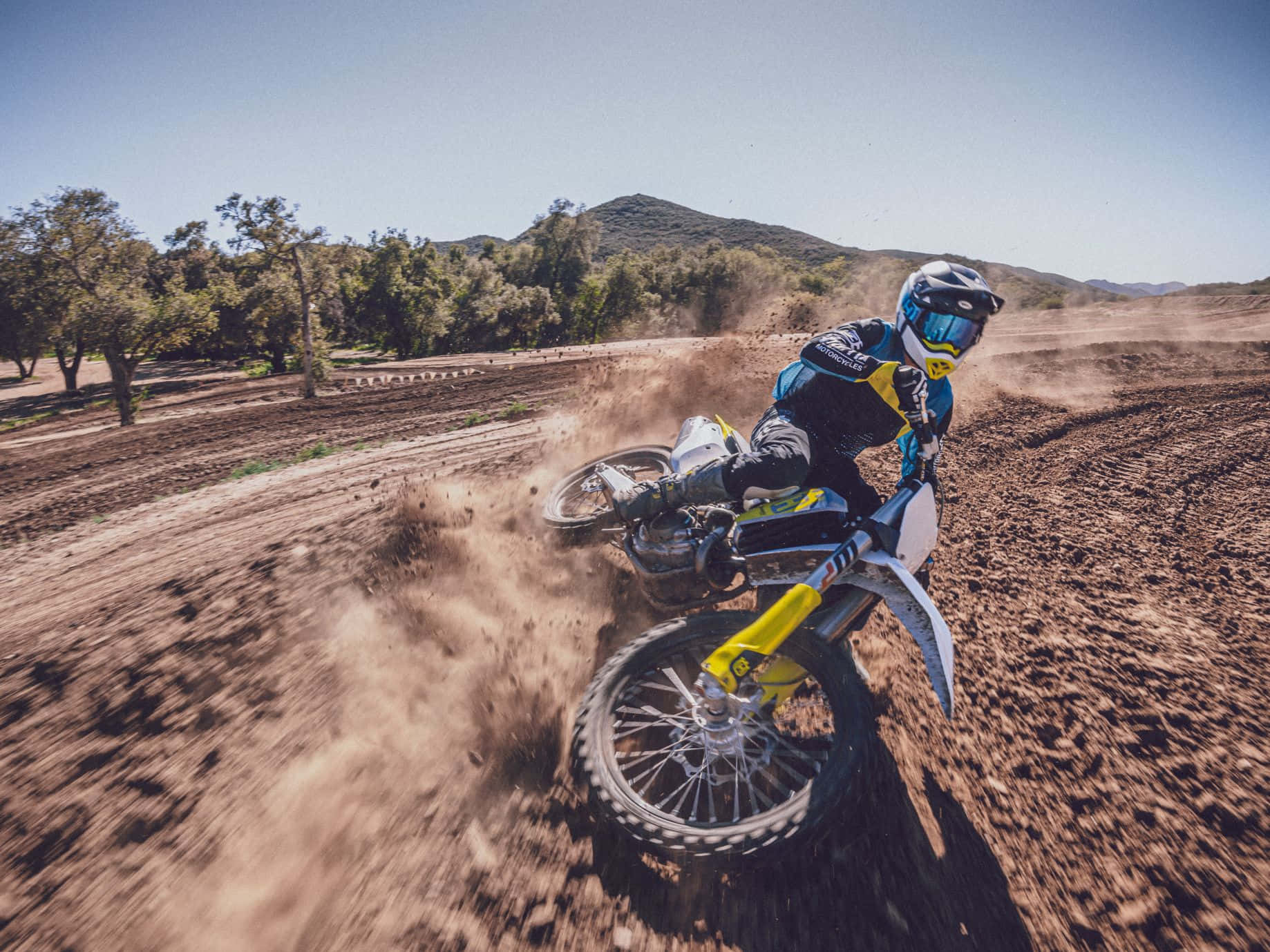 Motocross 桌布 壁紙 — 一位越野摩托車手在泥土賽道上傾身過急彎，在晴朗藍天下揚起塵土。