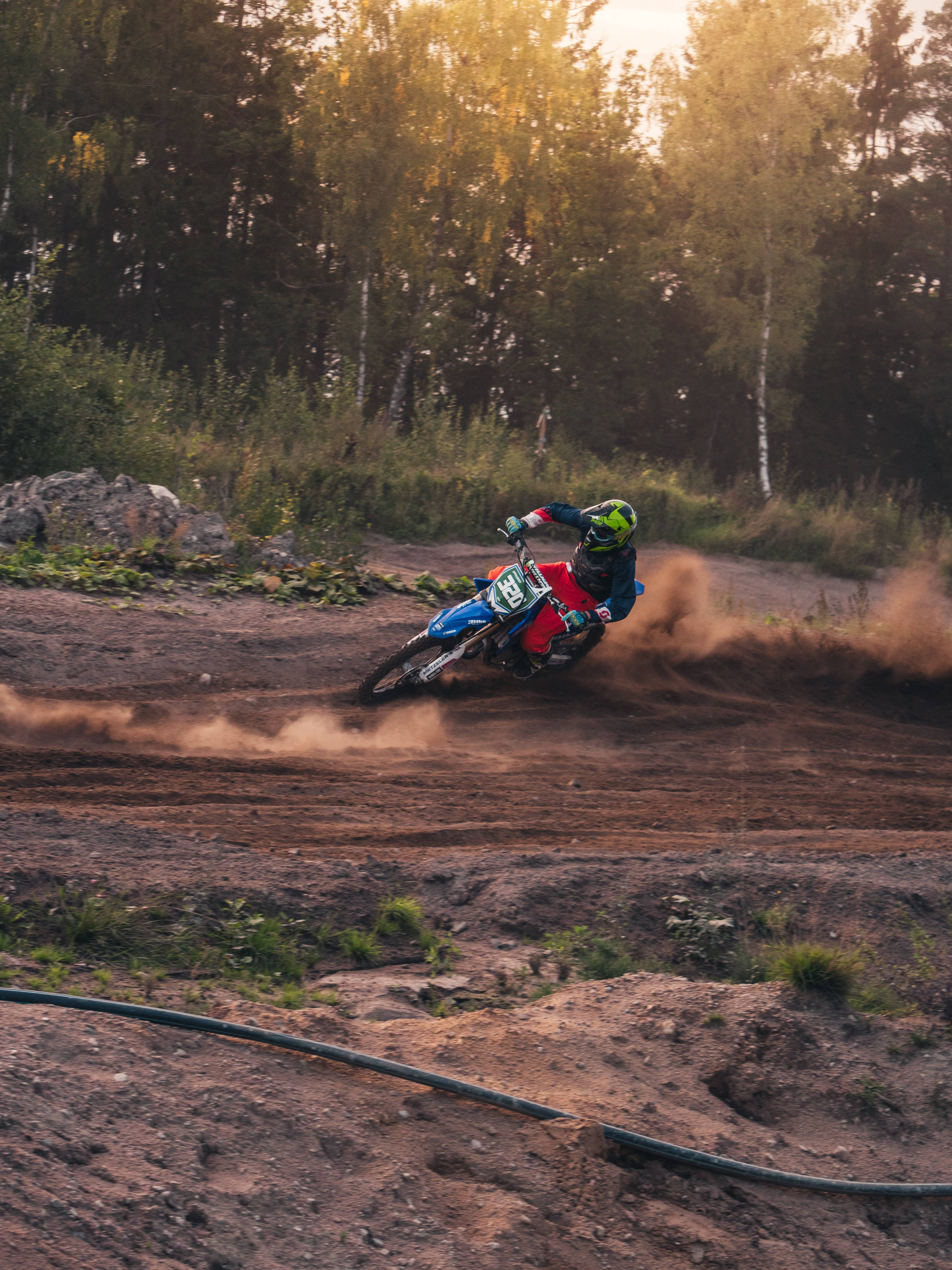 Dirtbike 桌布 壁紙 — 一位越野摩托車手在泥地上急轉彎，在金色夕陽下揚起塵土。