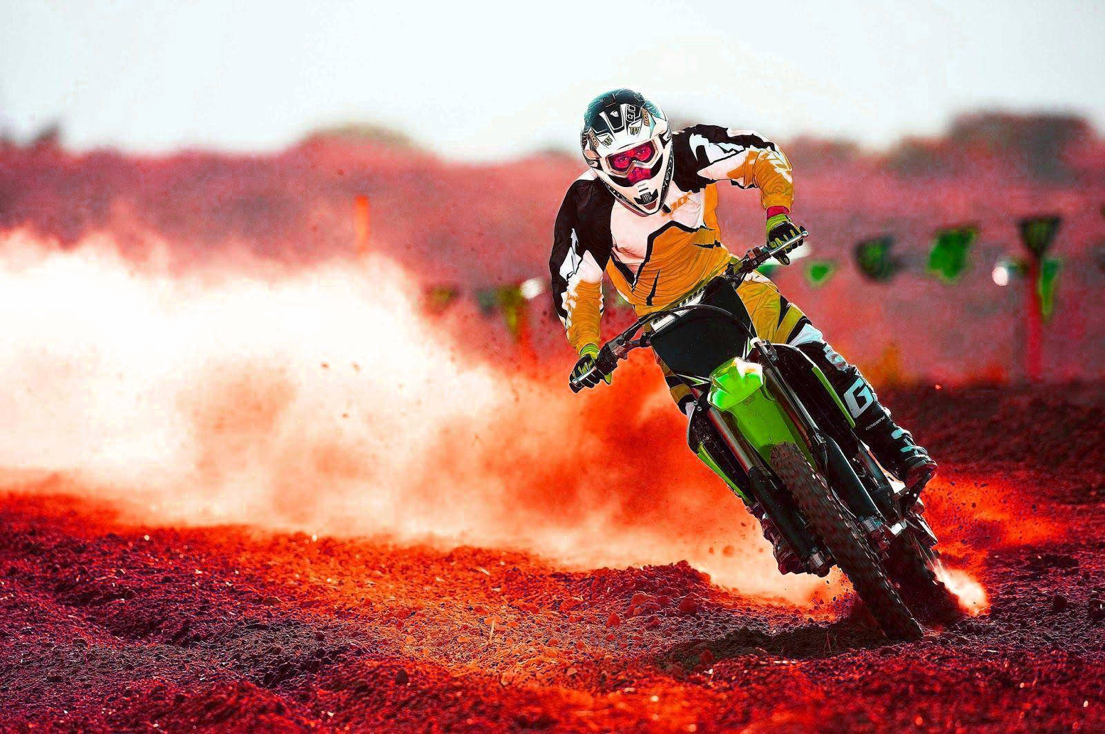 motorbike 桌布 壁紙 — 一位越野摩托車手在泥地賽道上傾斜入彎，在明亮的日光下揚起紅色塵土。