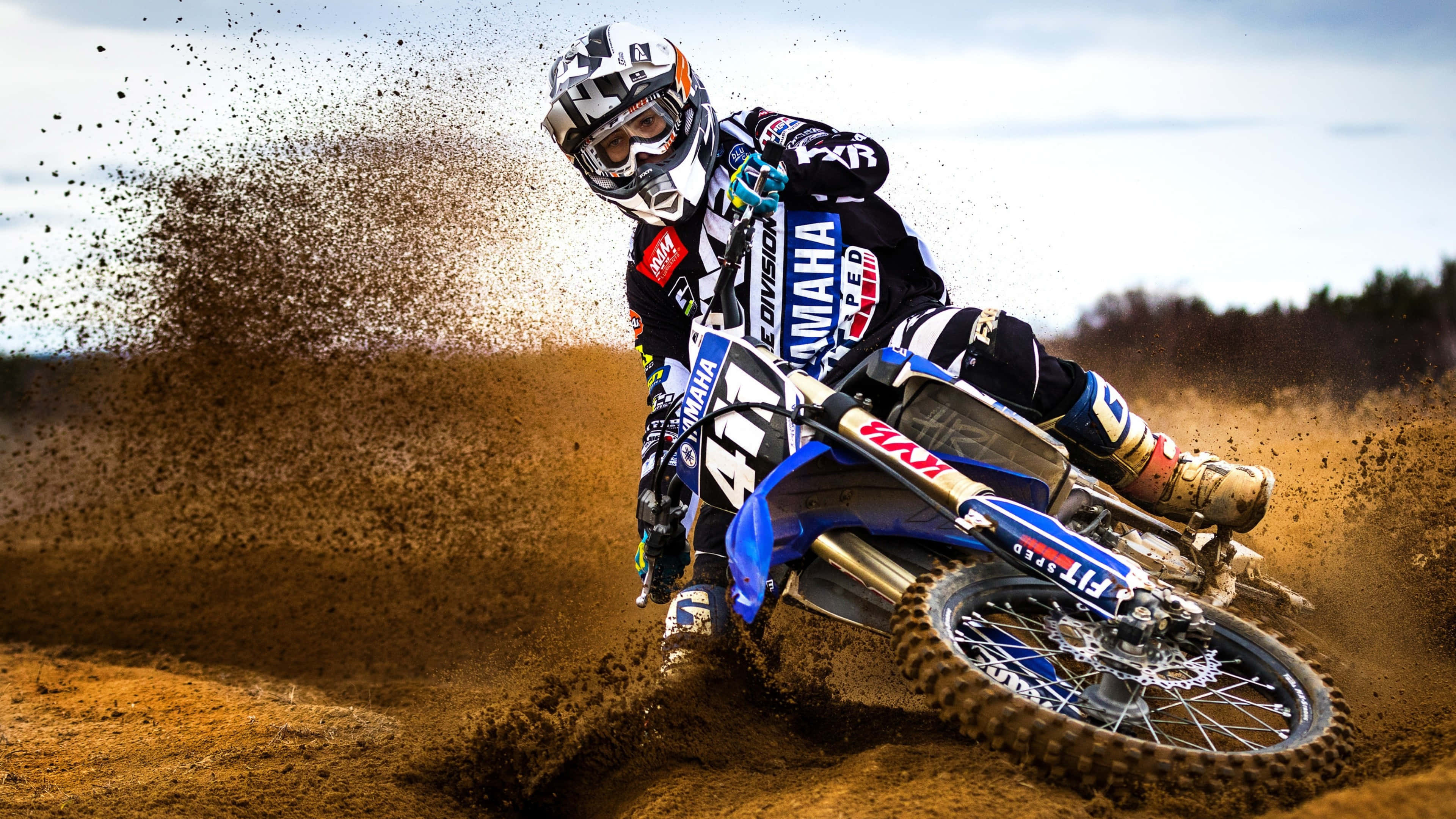 Motocross 桌布 壁紙 — 一位越野摩托車手在藍色Yamaha摩托車上傾斜入彎，在陽光明媚的戶外賽道上揚起泥土。