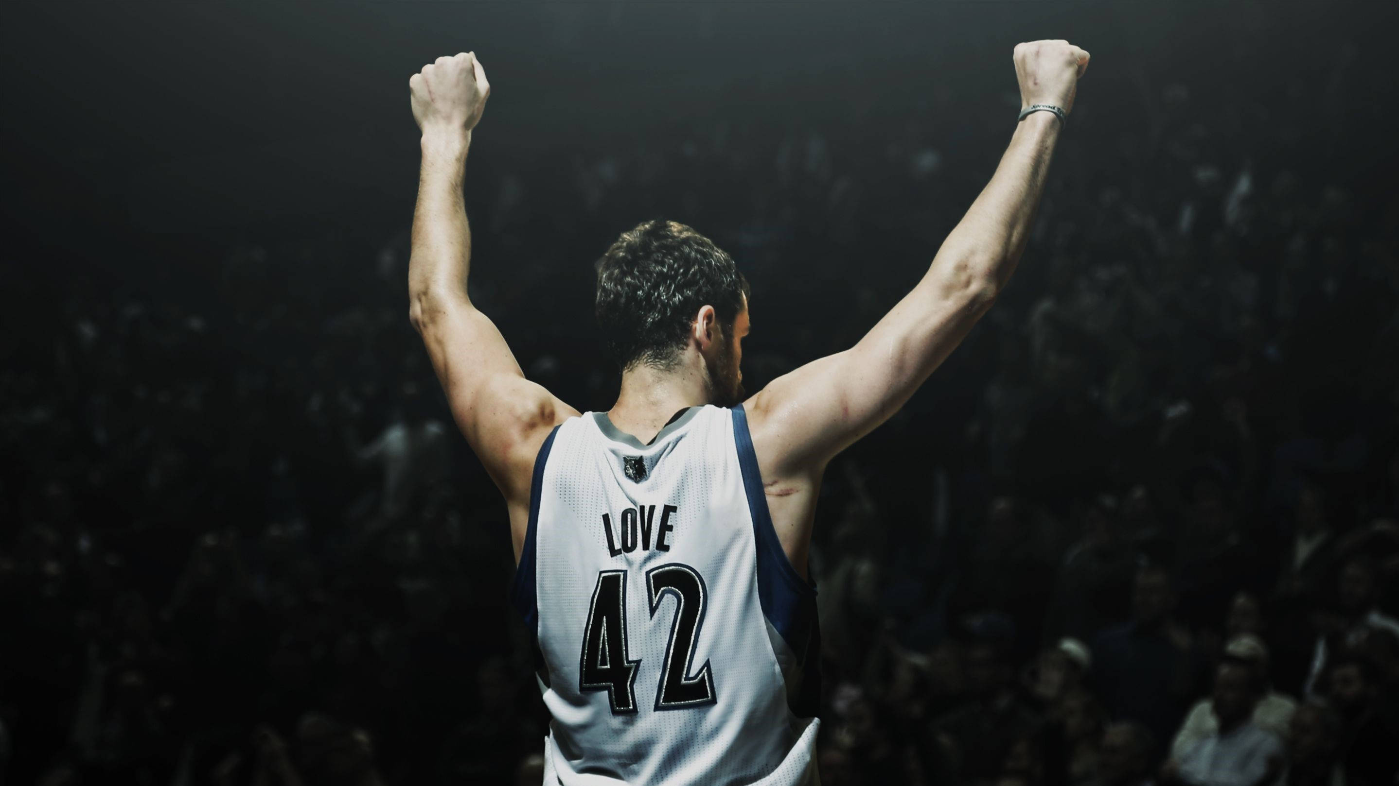Kevin Love 桌布 壁紙 — 一位身穿42號球衣的籃球運動員在燈光昏暗的場館中高舉拳頭慶祝勝利，人群歡呼。