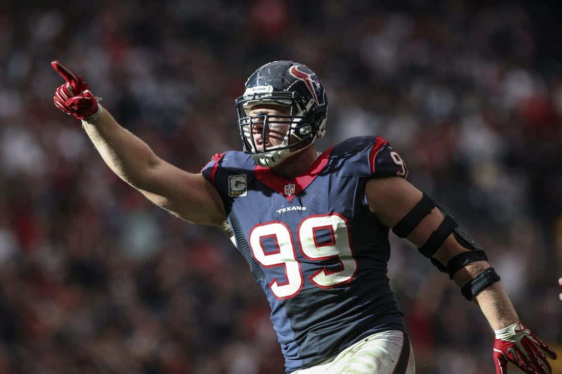 Jj Watt 桌布 壁紙 — 一位身穿99號球衣的休士頓德州人美式足球員，在陽光明媚的球場上伸展手臂向上指著慶祝。