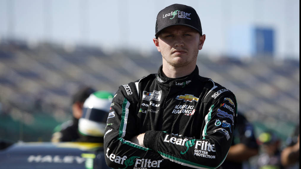 Racing 桌布 壁紙 — 一位身穿Leaf Filter賽車服的NASCAR車手在陽光明媚的賽道上自信地交叉雙臂站立。