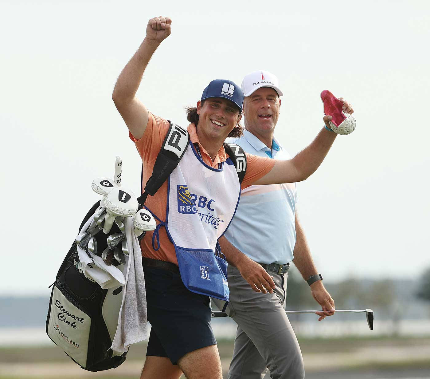 運動 桌布 壁紙 — 一位身穿RBC Heritage背心的高爾夫球手欣喜若狂地舉起拳頭慶祝勝利，他的球童在旁邊微笑著，手持高爾夫球桿和手套。