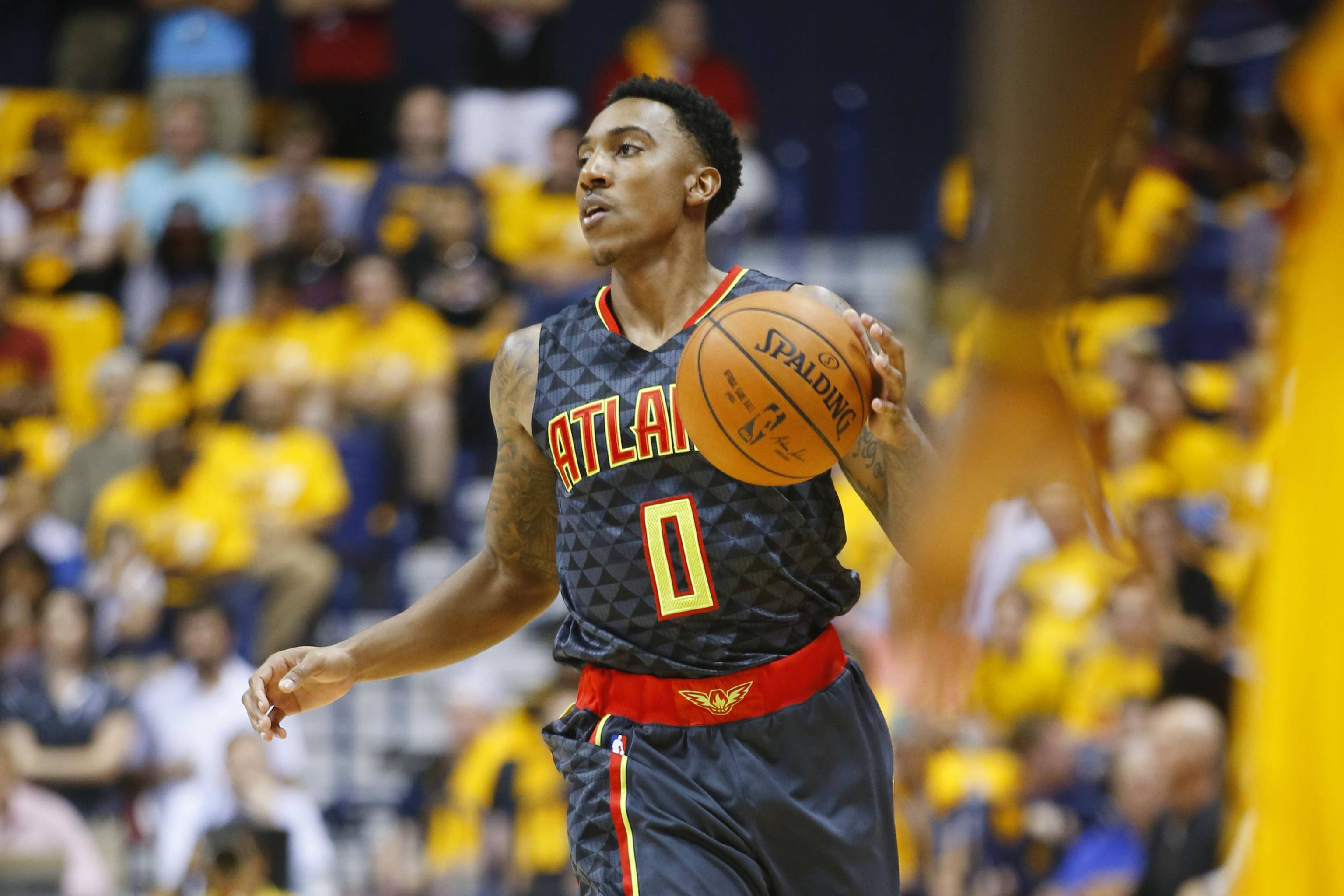 Hawks 桌布 壁紙 — 一位身穿亞特蘭大球衣的籃球運動員在比賽中手持 Spalding 籃球，神情專注，背景是模糊的黃衣球迷人群。