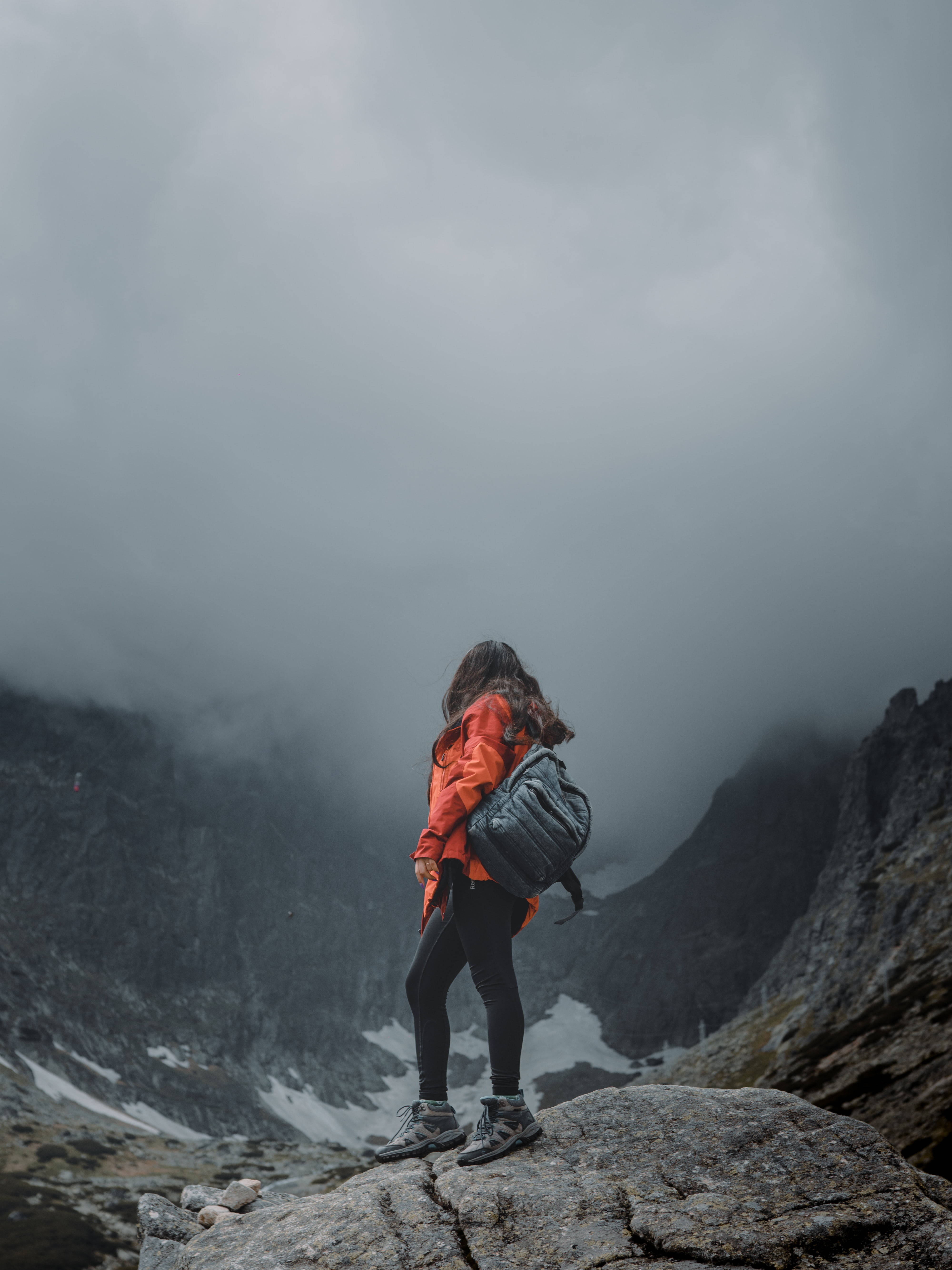 Hiking 桌布 壁紙 — 一位身穿亮橙色外套的孤獨遠足者，站在雲霧繚繞的山頂上，俯瞰著雲層籠罩的崎嶇山谷。