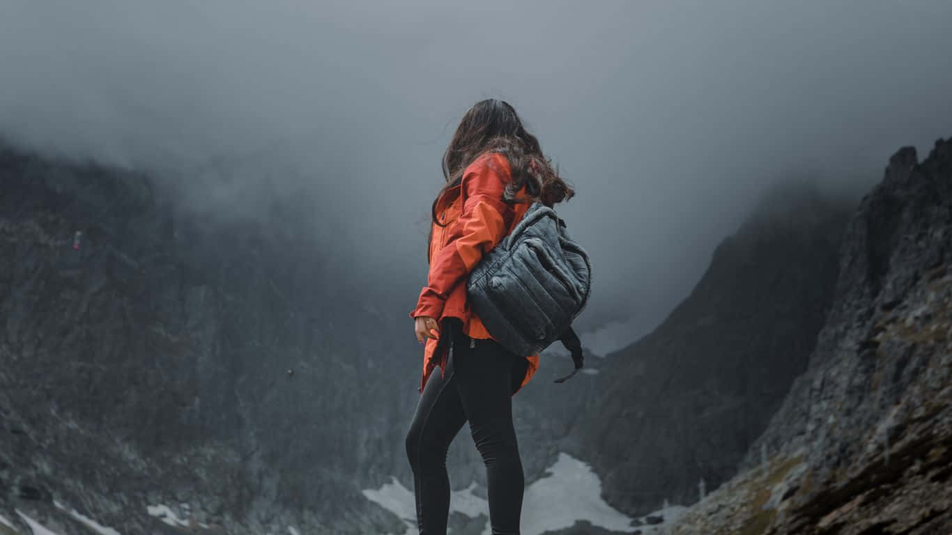 山景 桌布 壁紙 — 一位身穿亮橙色外套的孤獨遠足者站在霧氣瀰漫的山脊上，俯瞰著霧氣籠罩、帶有雪斑的山谷。