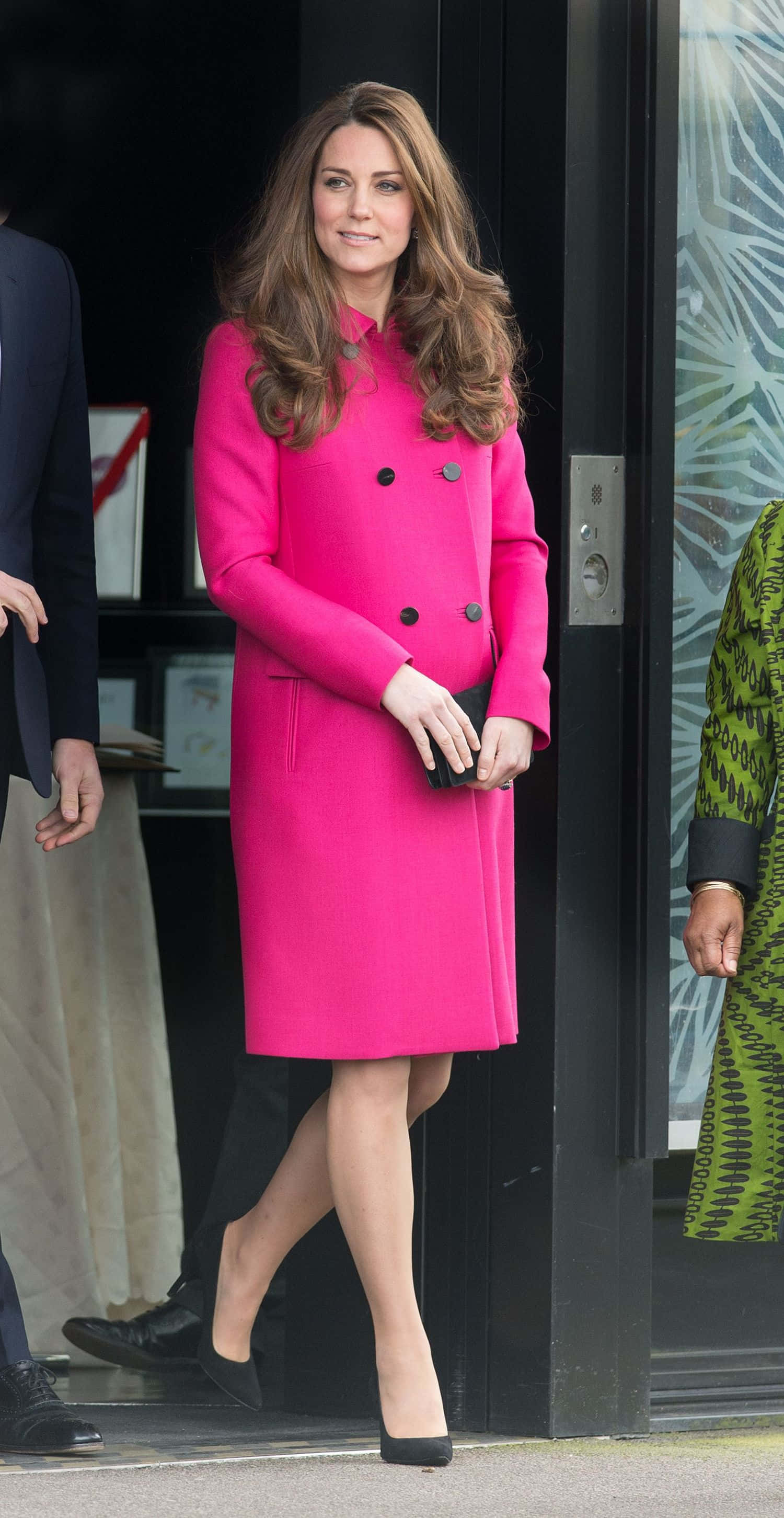 Pink Coat 桌布 壁紙 — 一位身穿亮粉色外套的女性帶著自信的微笑走過現代化的門口。