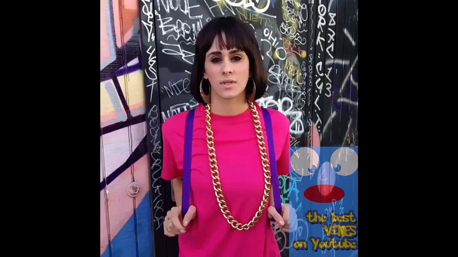 Funny Dora 桌布 壁紙 — 一位身穿亮粉色襯衫和金色鏈條的女性自信地站在色彩繽紛的塗鴉牆前。