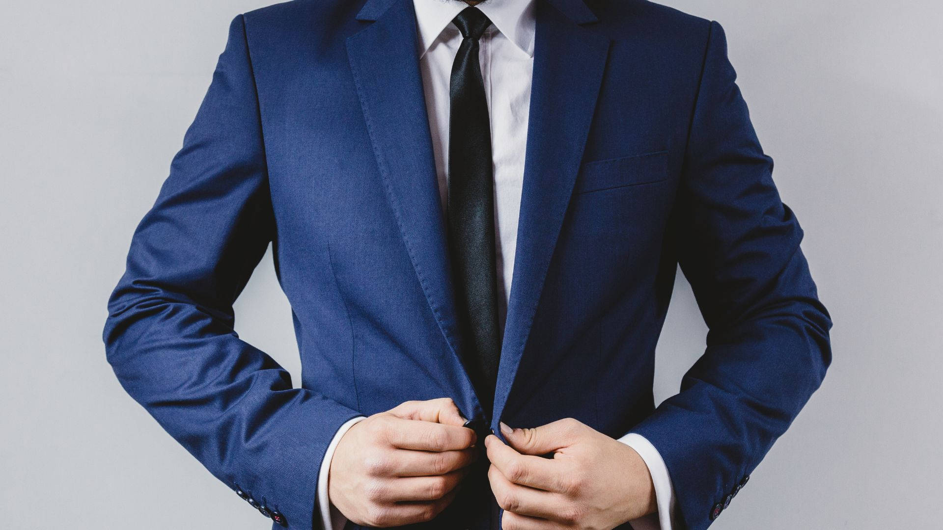 suit 桌布 壁紙 — 一位身穿亮藍色西裝的男人在灰色中性背景前扣上外套的鈕扣。
