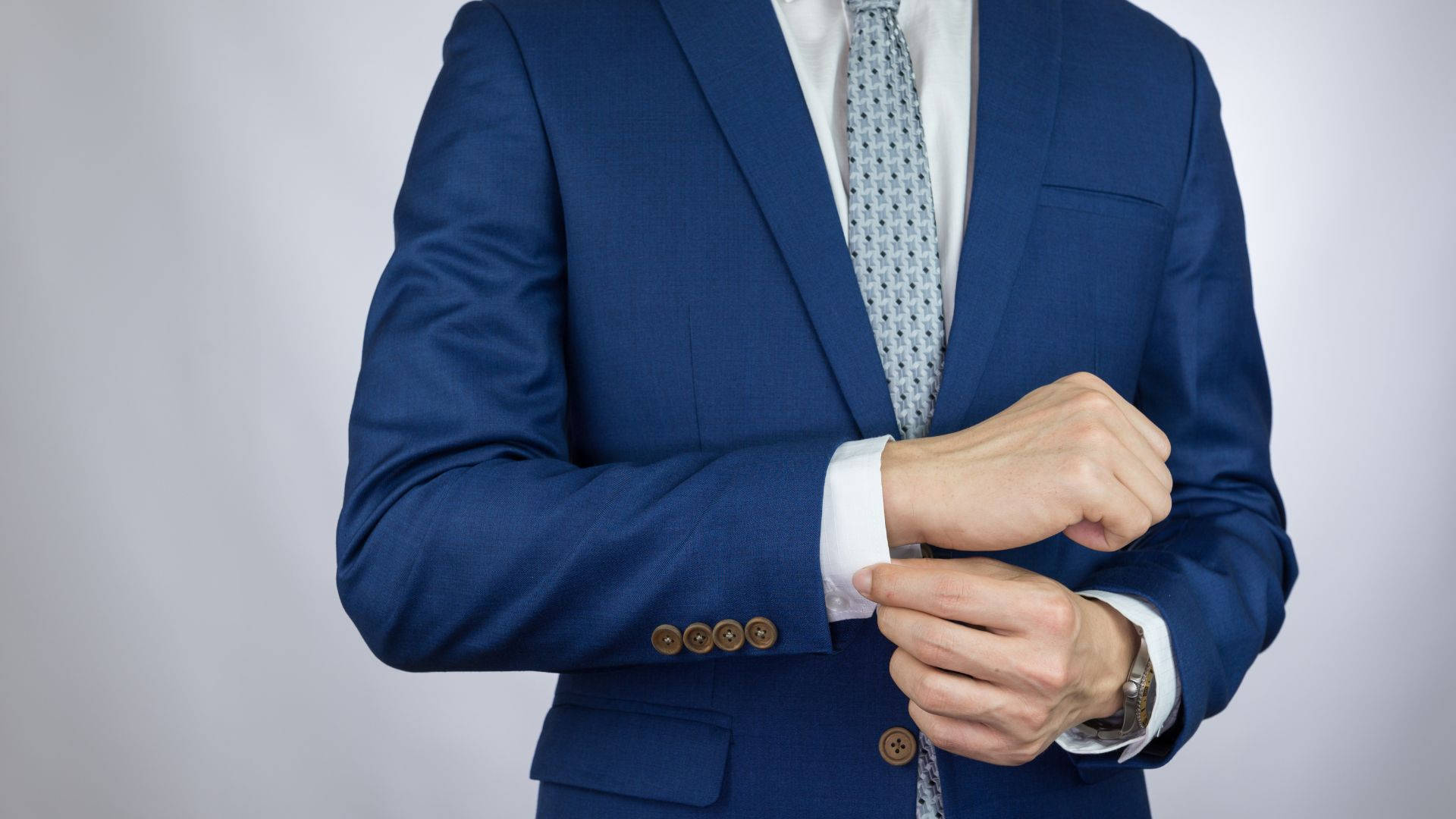 suit 桌布 壁紙 — 一位身穿亮藍色西裝的男士在中性工作室背景前調整他的袖扣。