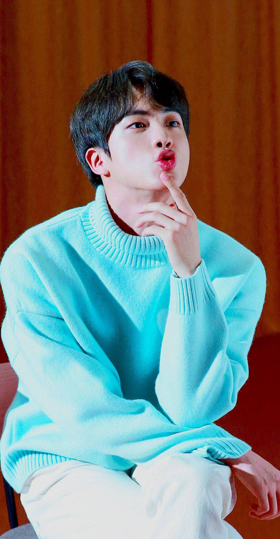 kim seok jin 桌布 壁紙 — 一位身穿亮青色毛衣的年輕男子，在溫暖的木質背景下，托腮嘟嘴。