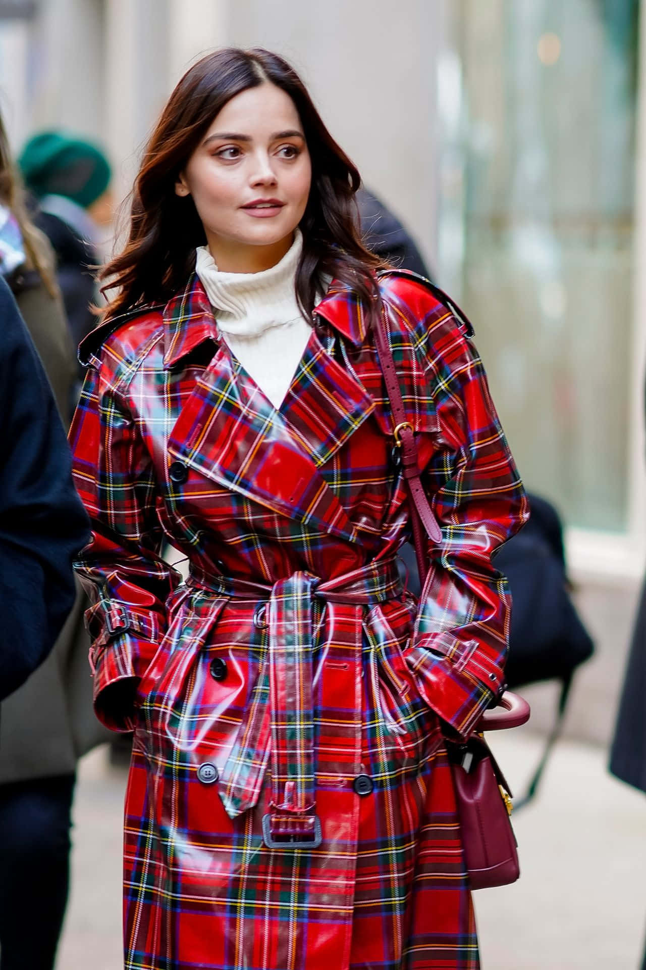 Jenna Coleman 桌布 壁紙 — 一位身穿亮面紅色格紋風衣的女性，自信地走過城市街道，手提一個栗色手袋。