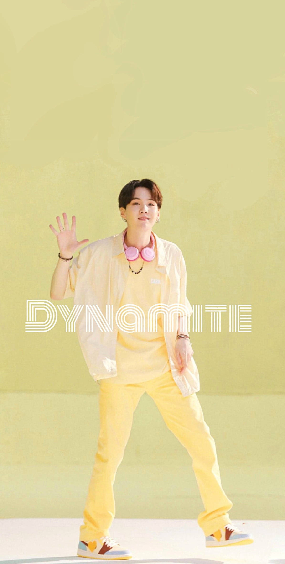 Bts Suga Aesthetic 桌布 壁紙 — 一位身穿亮黃色服裝的年輕男子在柔和的綠色背景上，帶有 'DYNAMITE' 文字疊加，愉快地揮手。