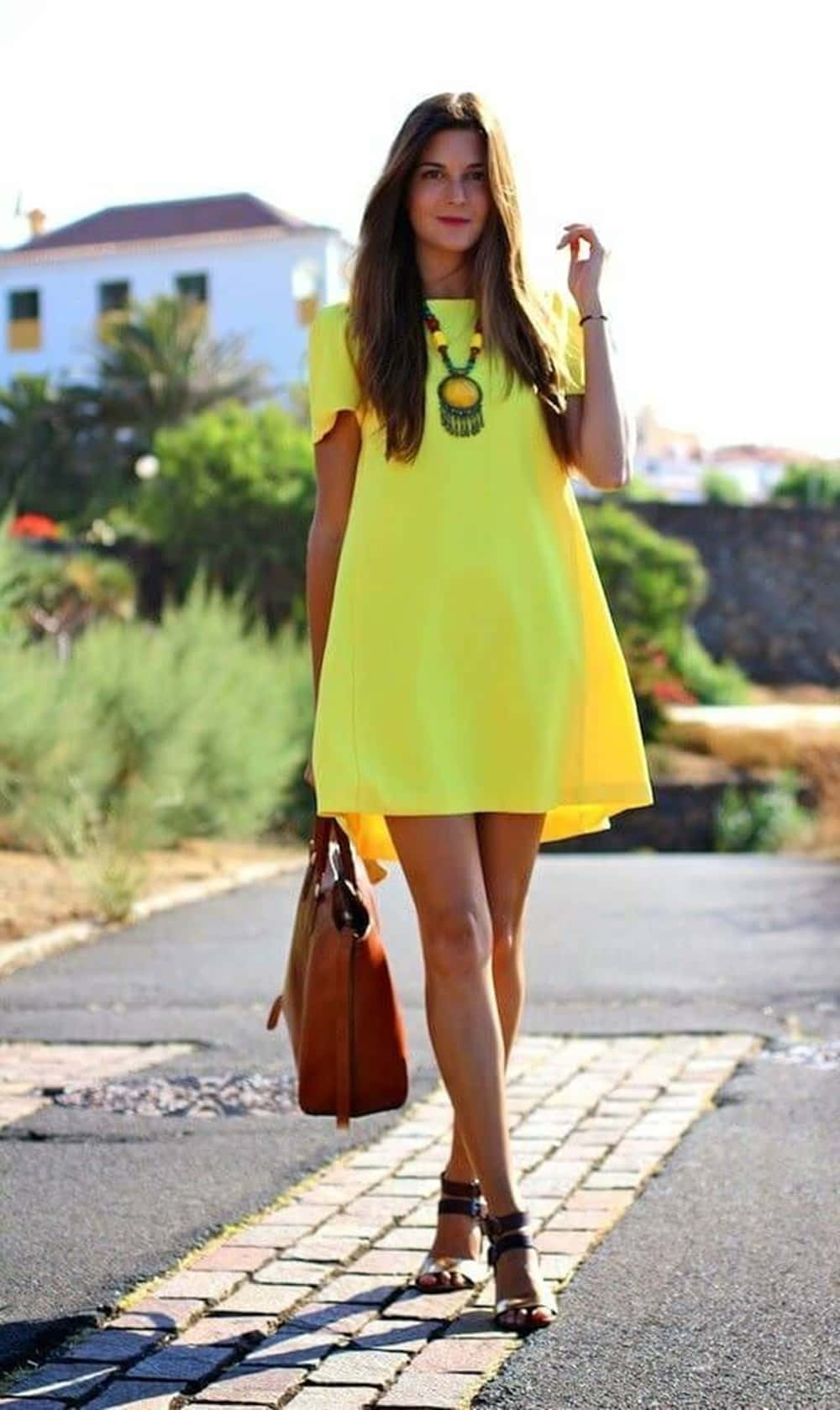 Yellow Fashion 桌布 壁紙 — 一位身穿亮黃色連衣裙的女性自信地走在陽光明媚的鵝卵石小徑上，背景是棕櫚樹和白色建築。