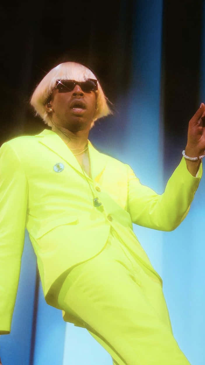 Tyler The Creator 4K 桌布 壁紙 — 一位身穿亮黃色霓虹套裝和白色鮑伯假髮的表演者在藍色舞台燈光下跳舞。