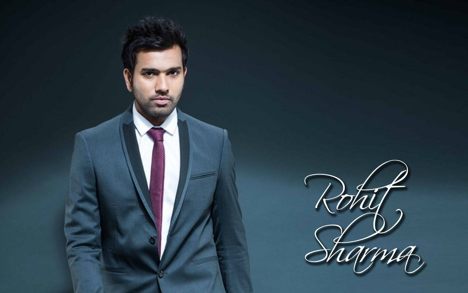 Rohit Sharma 桌布 壁紙 — 一位身穿俐落灰色西裝、繫著酒紅色領帶的男子，自信地站在深色漸變背景前，他的名字以優雅的白色草書呈現。