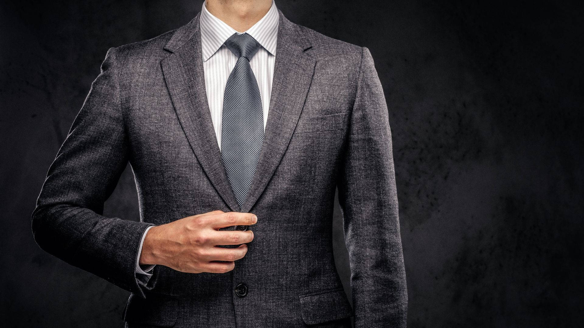 suit 桌布 壁紙 — 一位身穿俐落灰色西裝的男子在深色紋理背景前調整領帶。