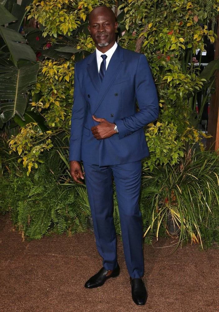 Celebrity 桌布 壁紙 — 一位身穿俐落藍色雙排扣西裝的男子，自信地站在茂密綠色樹葉背景前。