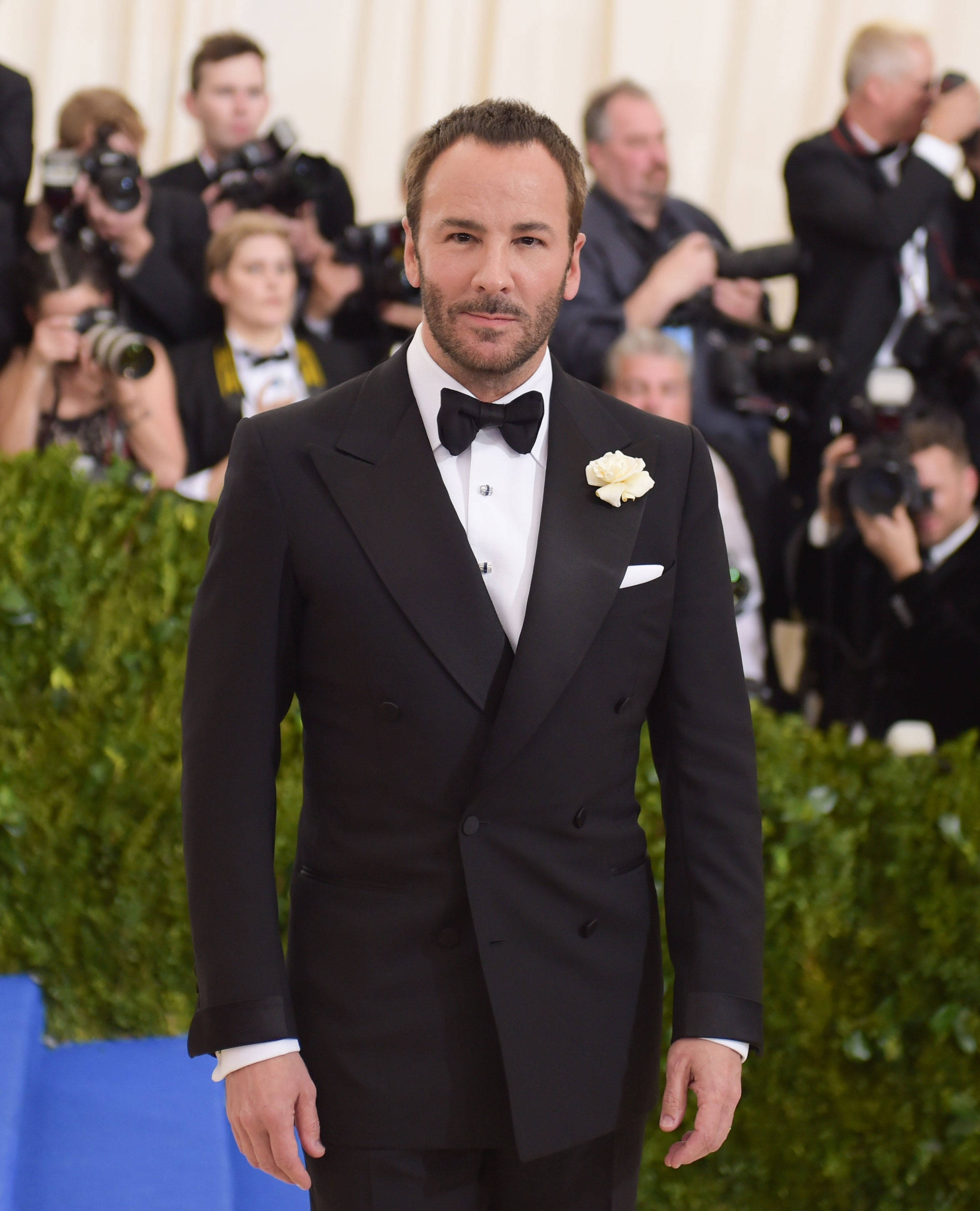 Celebrity 桌布 壁紙 — 一位身穿俐落黑色燕尾服、佩戴白色玫瑰胸花的男士，自信地站在藍色地毯上，被攝影師包圍。