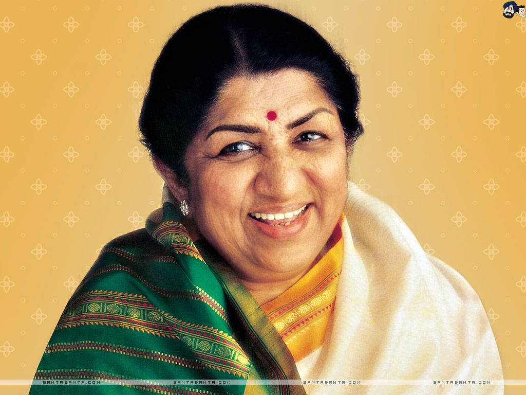 Lata Mangeshkar 桌布 壁紙 — 一位身穿傳統印度服飾的容光煥發的女性，在圖案化的金黃色背景下溫暖地微笑。