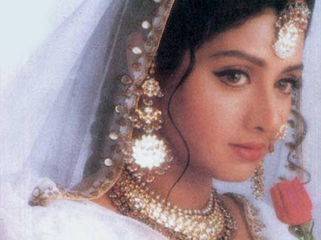 Sridevi 桌布 壁紙 — 一位身穿傳統新娘禮服、佩戴精緻黃金首飾和白色頭紗、手持紅玫瑰的女子的特寫肖像。