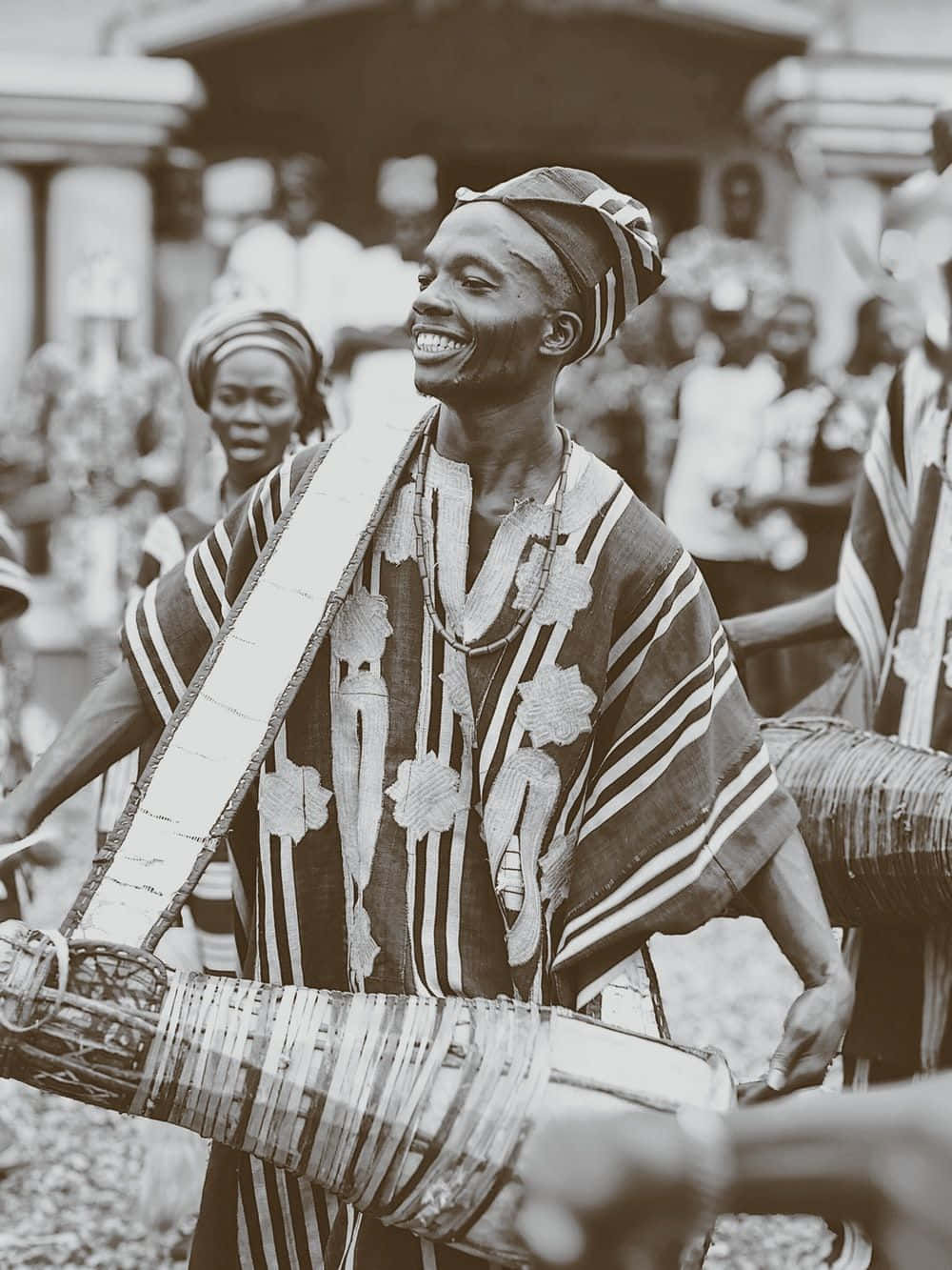 African Culture 桌布 壁紙 — 一位身穿傳統條紋服飾的快樂男子，在文化聚會中微笑著演奏大型手鼓。