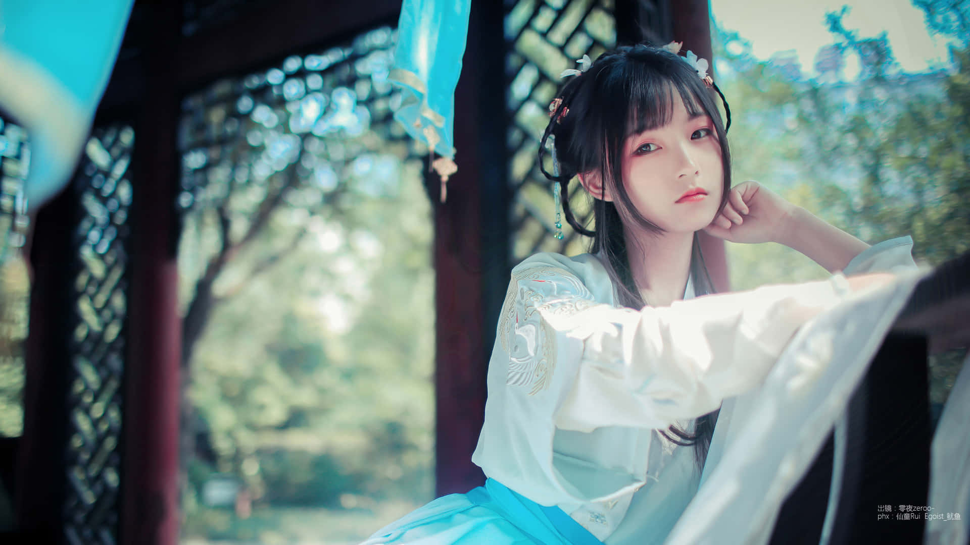Sitting Alone 桌布 壁紙 — 一位身穿傳統白色和藍色漢服的年輕女子在木亭內優雅地擺姿勢，透過格子窗可以看到茂密的綠色植物。