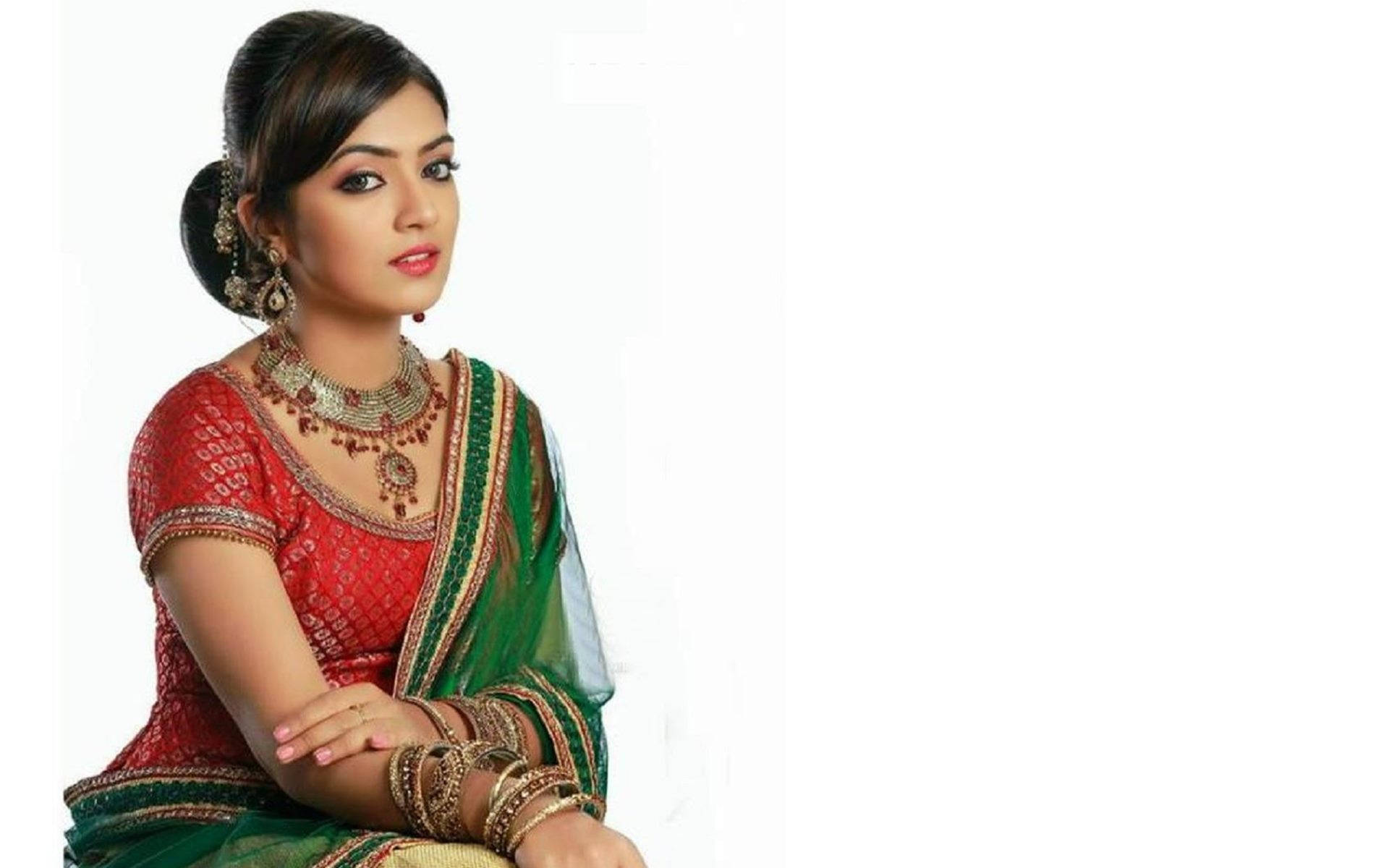 Indian 桌布 壁紙 — 一位身穿傳統紅綠色印度服飾、飾以黃金珠寶的女性，在純白背景前優雅地擺姿勢。