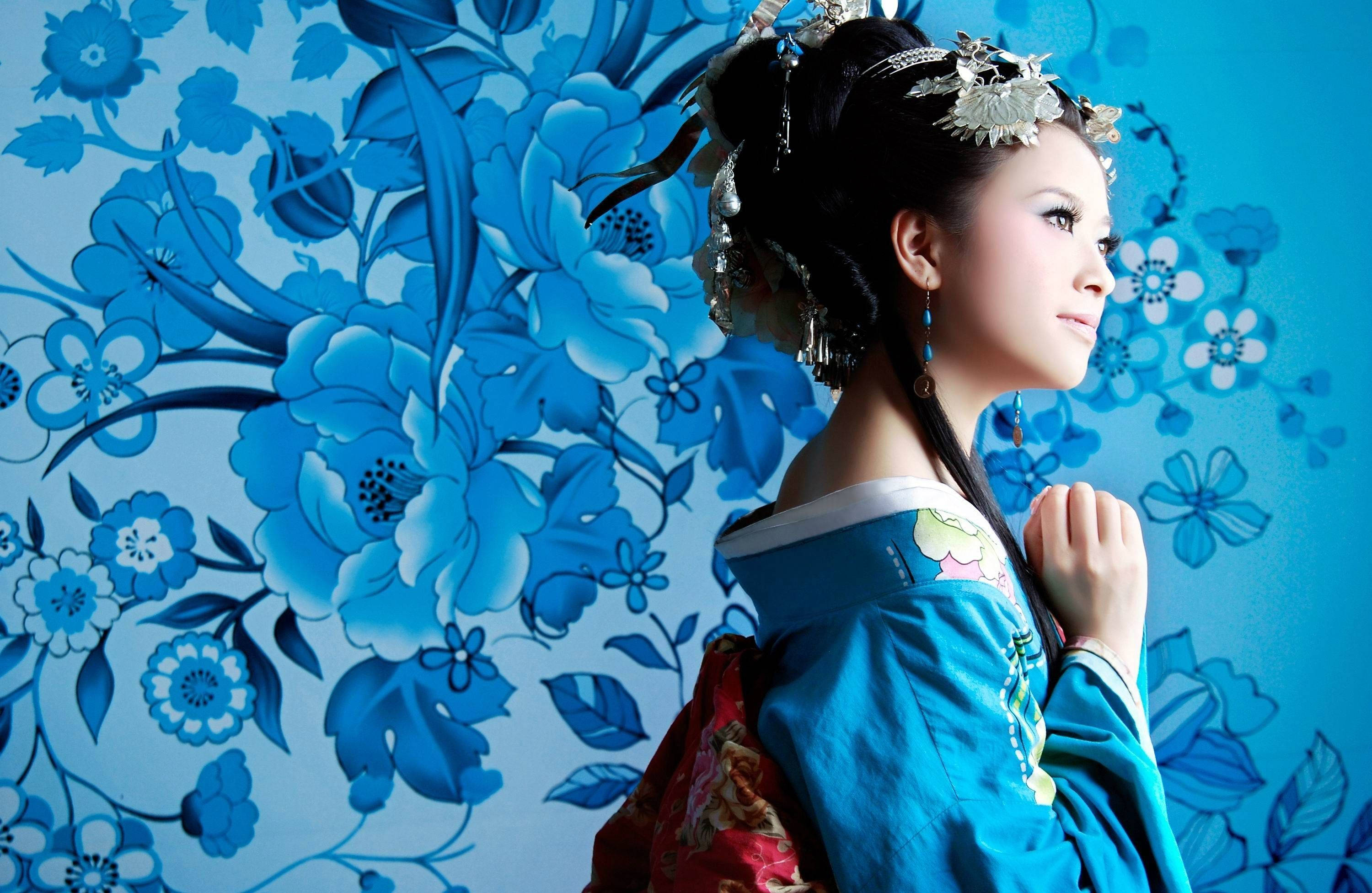 漂亮美學 桌布 壁紙 — 一位身穿傳統藍紅服飾的女性，優雅地站在鮮豔的藍色花卉壁紙背景前。