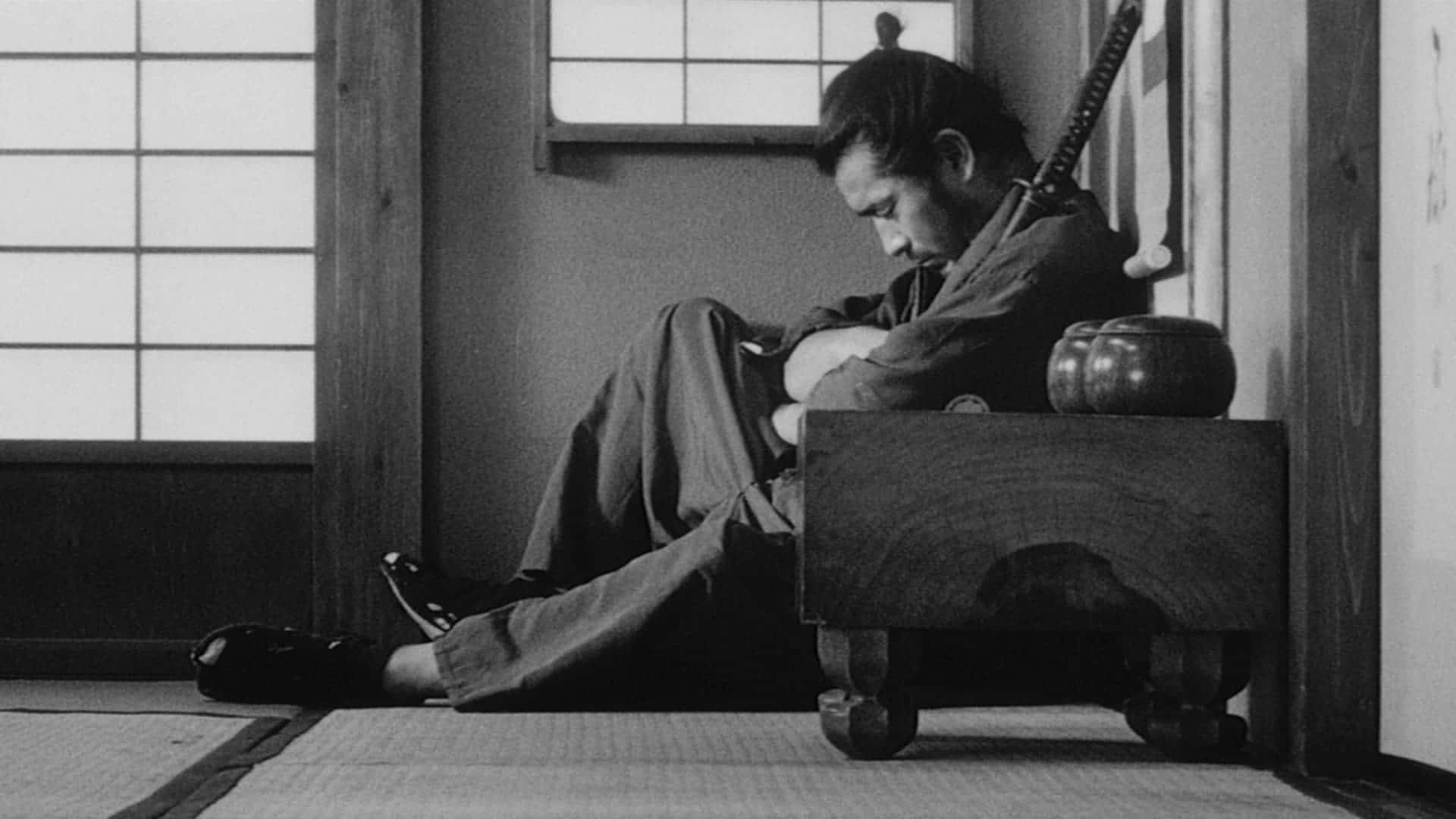 Samurai Movies 桌布 壁紙 — 一位身穿傳統長袍的武士，坐在簡約日式房間的木凳上，隔著障子屏風沉思。
