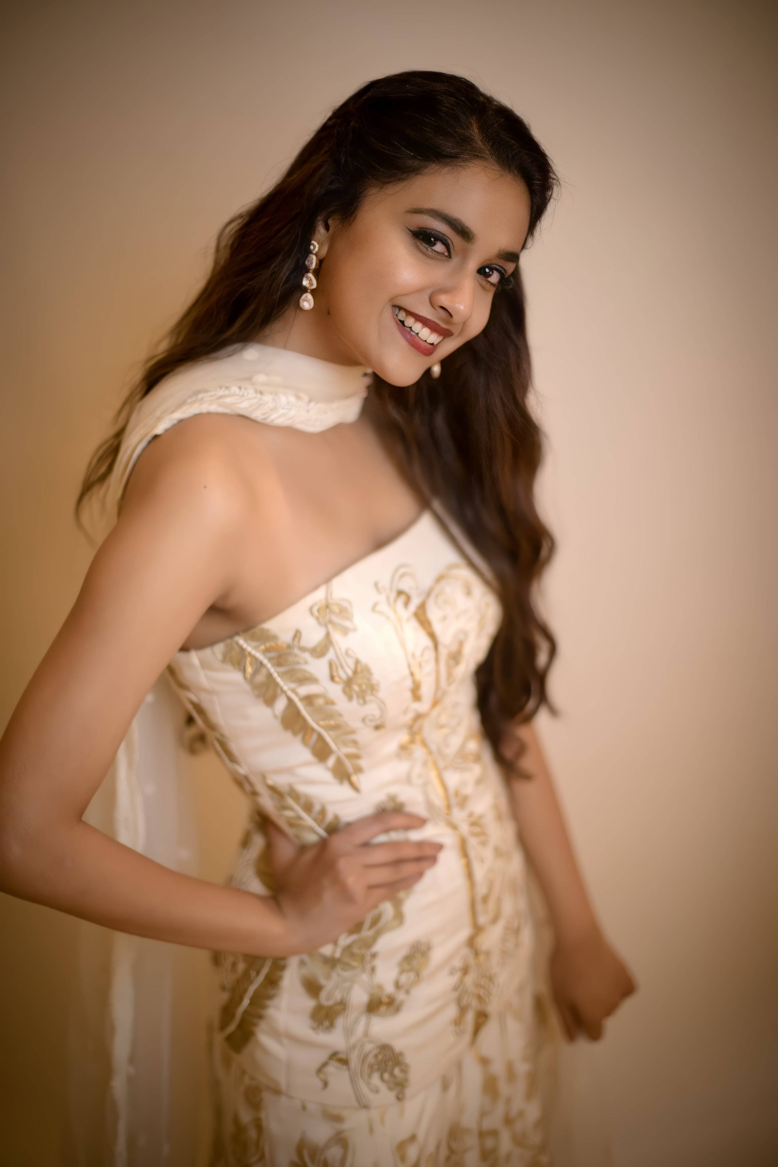 telugu 桌布 壁紙 — 一位身穿優雅奶油色和金色刺繡長袍的容光煥發的女性，在柔和的米色背景下溫暖地微笑。