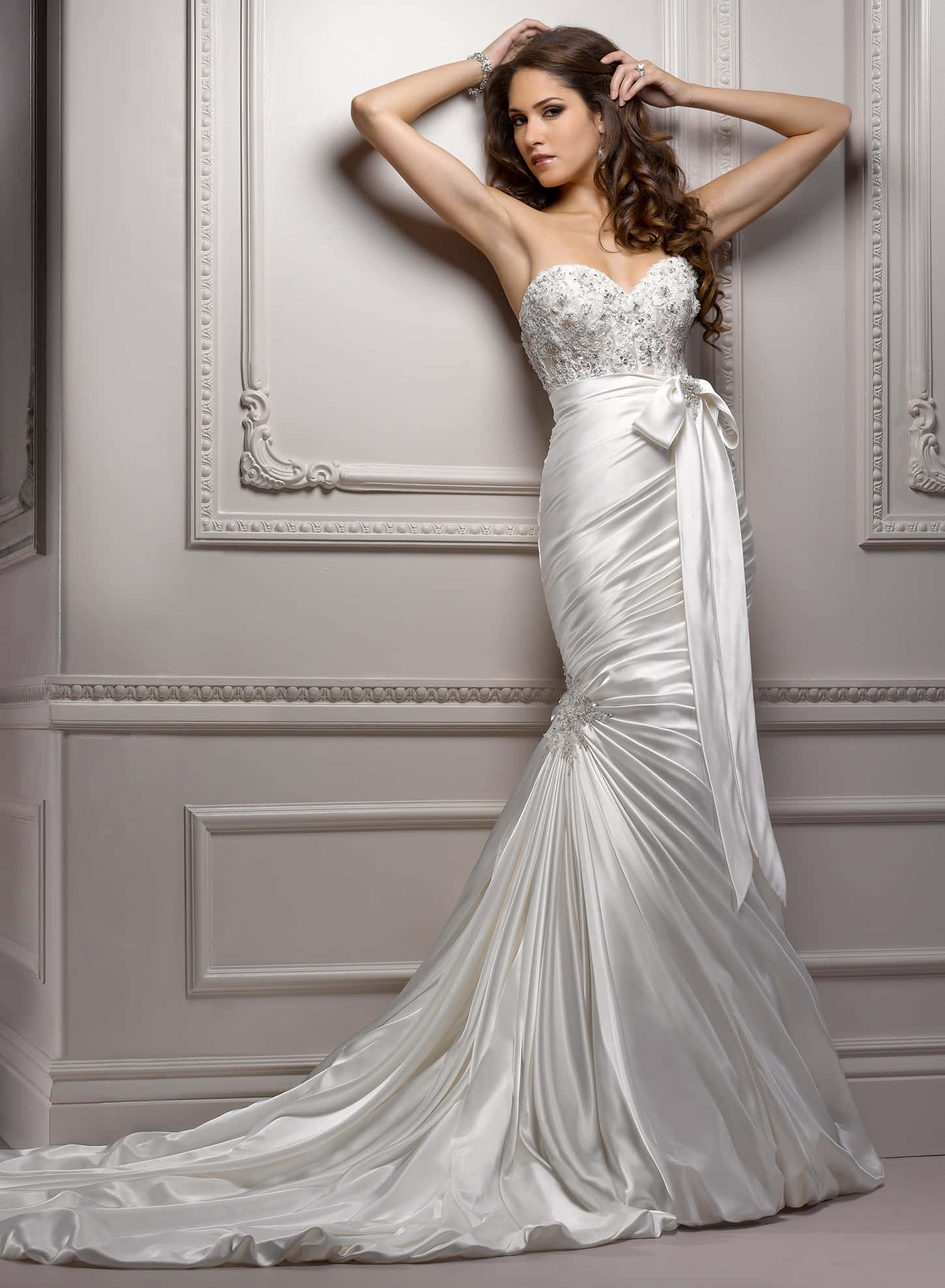 Wedding Gown 桌布 壁紙 — 一位身穿優雅白色美人魚婚紗（蕾絲上身配緞面拖尾）的女性，在經典灰色牆壁前優雅地擺姿勢。