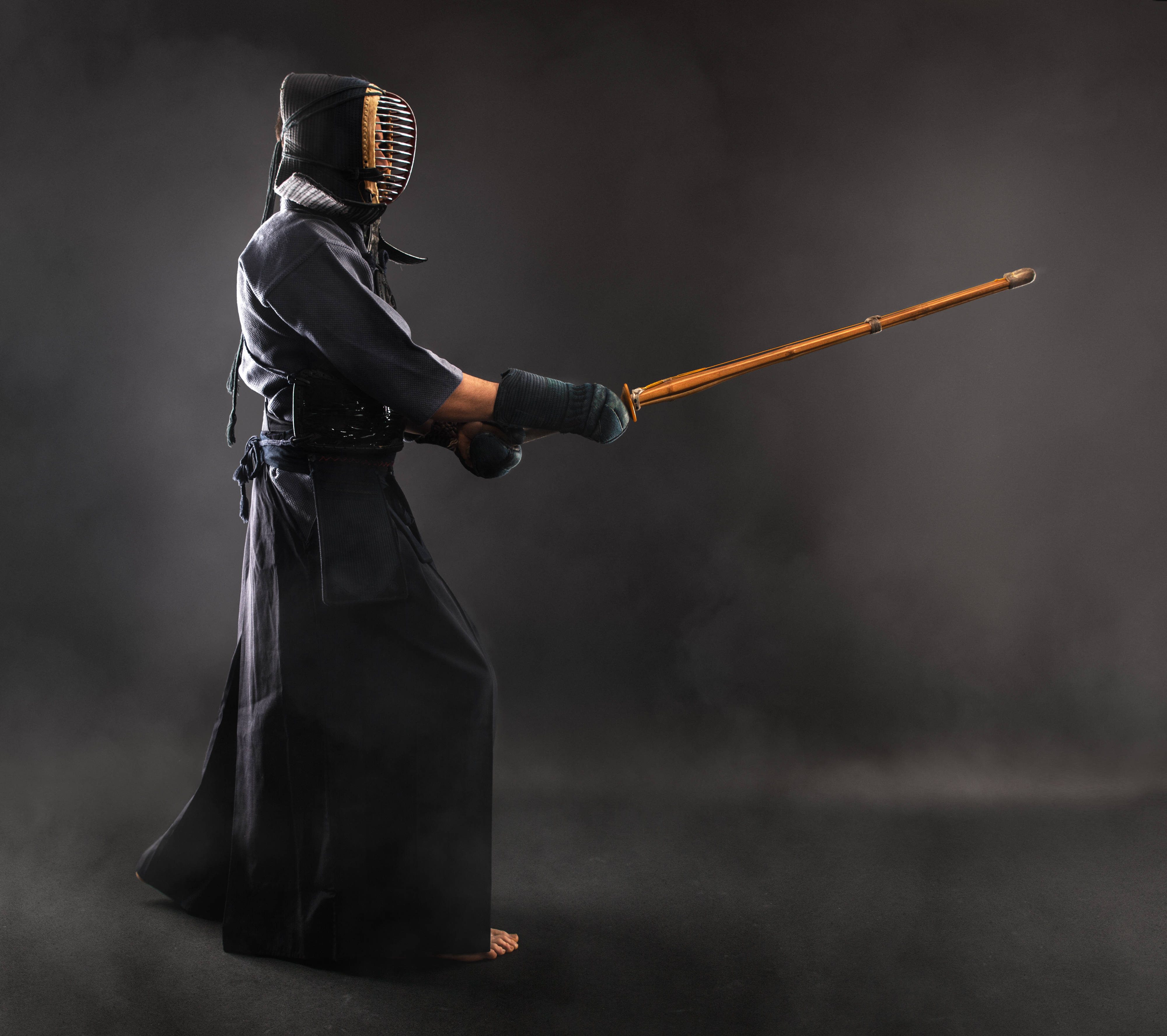 sword 桌布 壁紙 — 一位身穿全副黑色盔甲的劍道練習者，在煙霧瀰漫的黑暗工作室背景下，手持竹劍擺出姿勢。