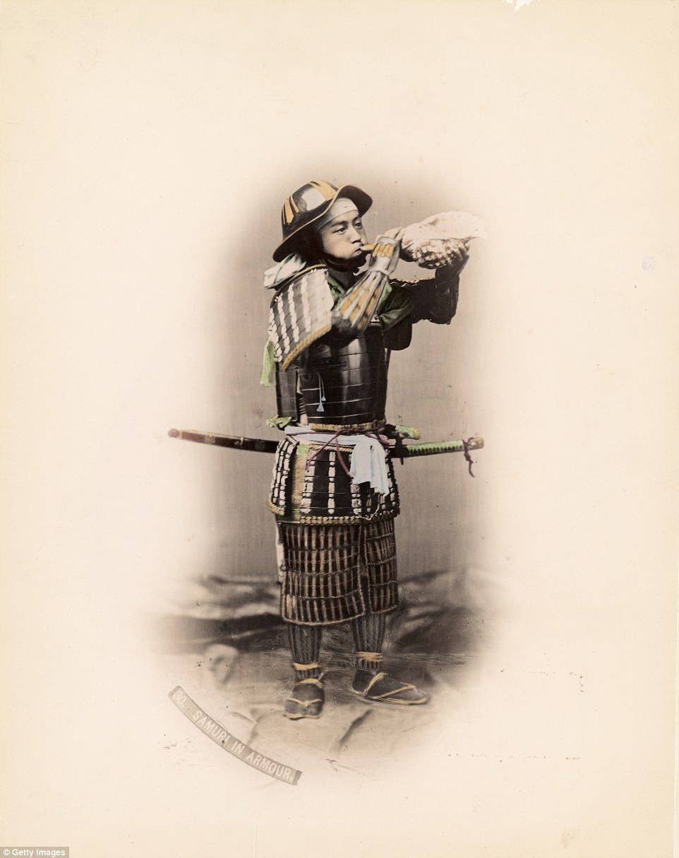Seppuku 桌布 壁紙 — 一位身穿全套傳統盔甲的武士，在樸素背景前手持扇子擺出姿勢，帶有復古攝影色調。