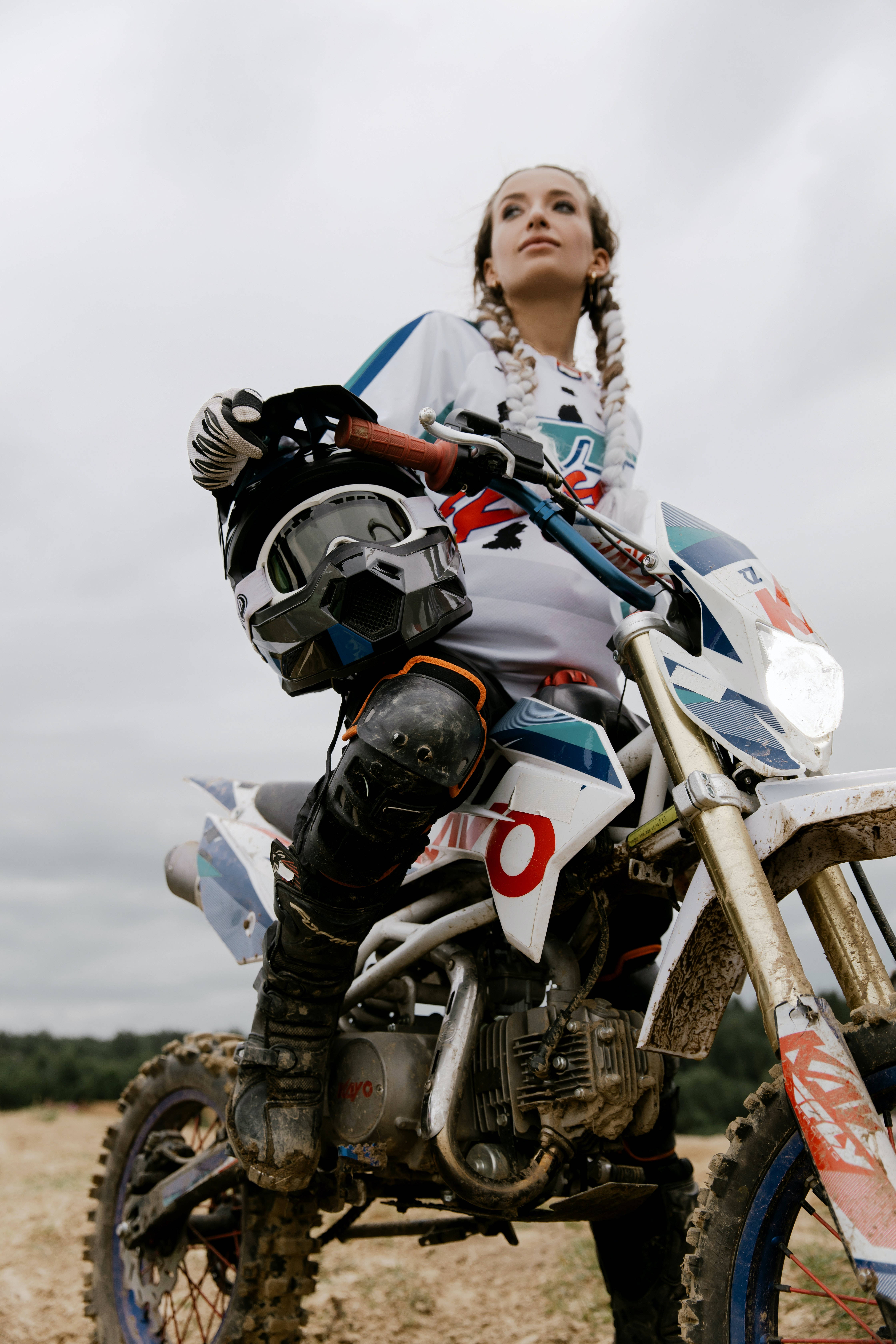 Dirtbike 桌布 壁紙 — 一位身穿全套裝備的女越野機車手坐在泥濘的機車上，仰望陰天。