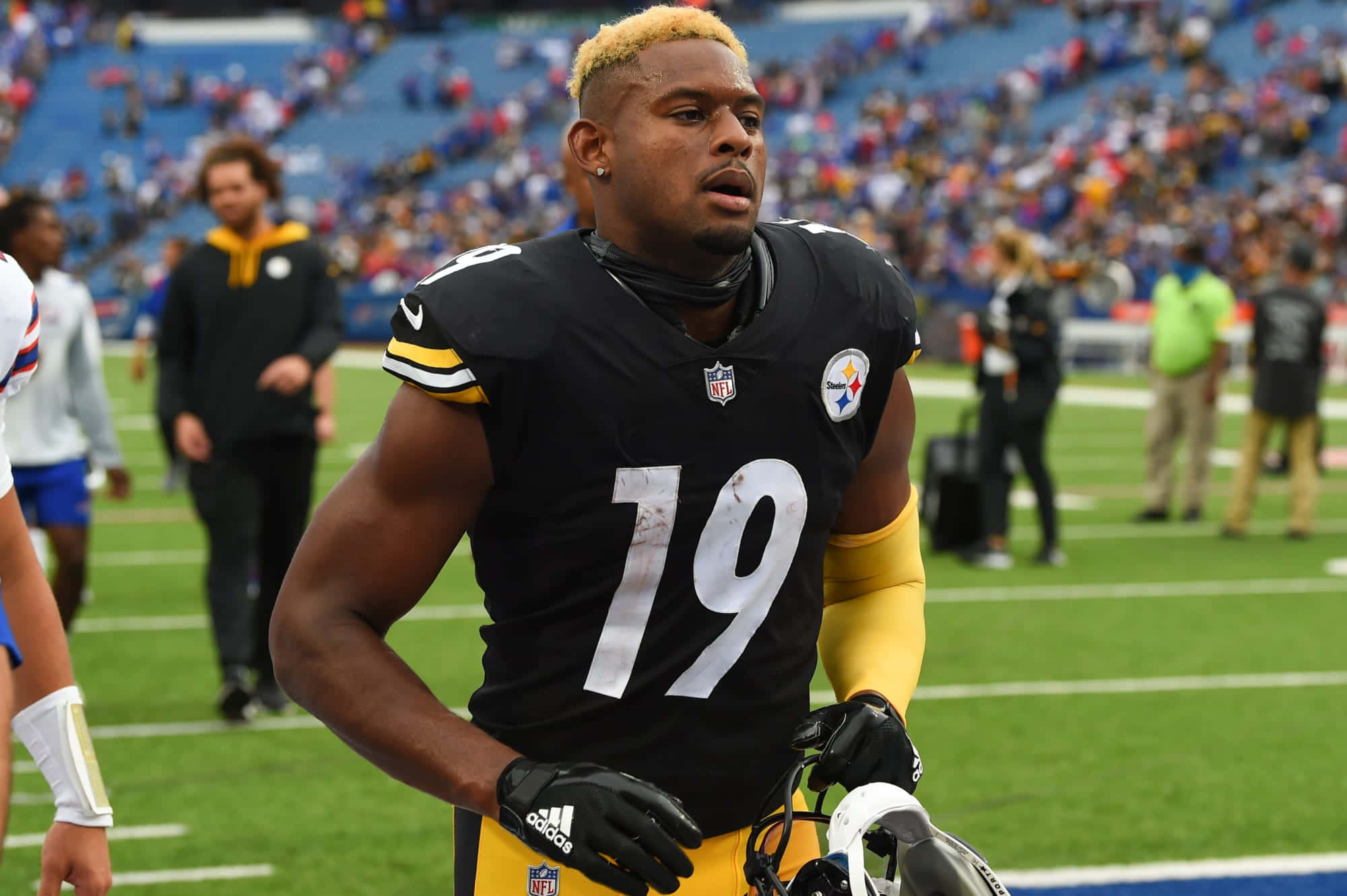 Juju Smith Schuster 桌布 壁紙 — 一位身穿匹茲堡鋼人隊19號球衣的美式足球員，站在陽光普照的綠色球場上，背景是體育場的觀眾。