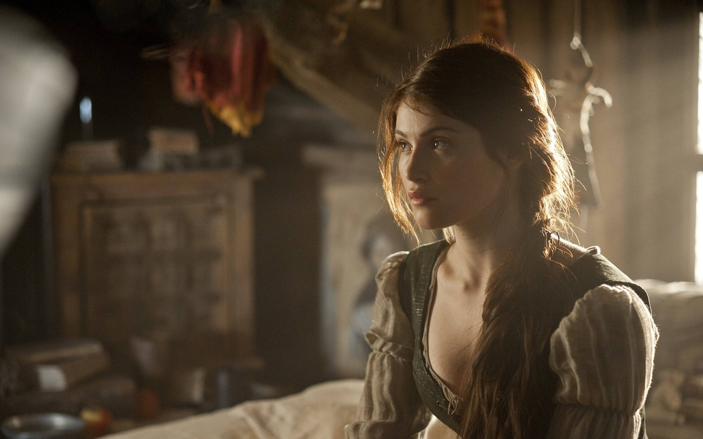 Gemma Arterton 桌布 壁紙 — 一位身穿古裝的女子在光線昏暗的鄉村房間裡若有所思地凝視著，溫暖的陽光透過窗戶照射進來。