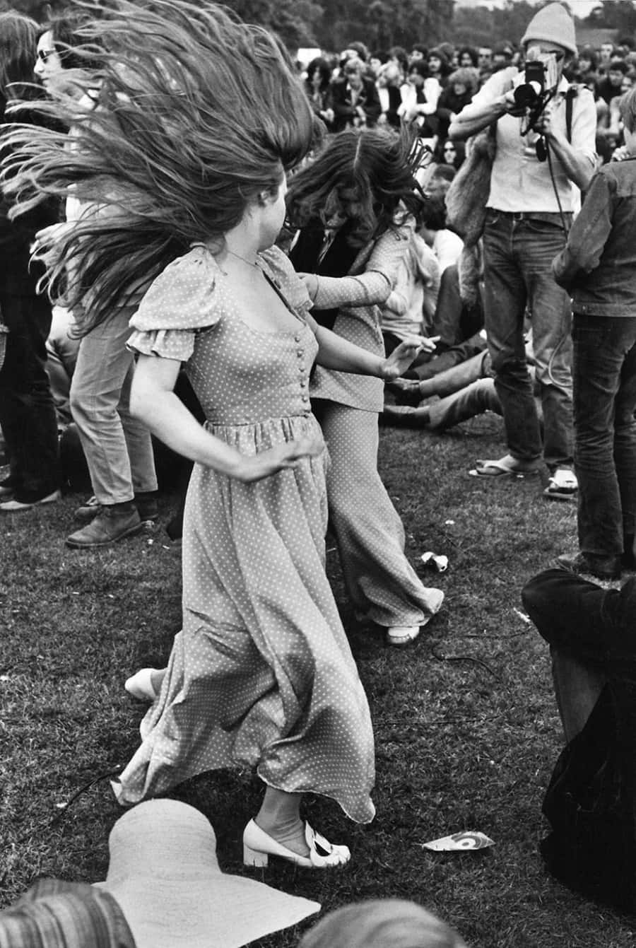 Woodstock 桌布 壁紙 — 一位身穿圓點裙的女子在戶外聚會中熱情起舞，頭髮飛揚，旋轉不停。