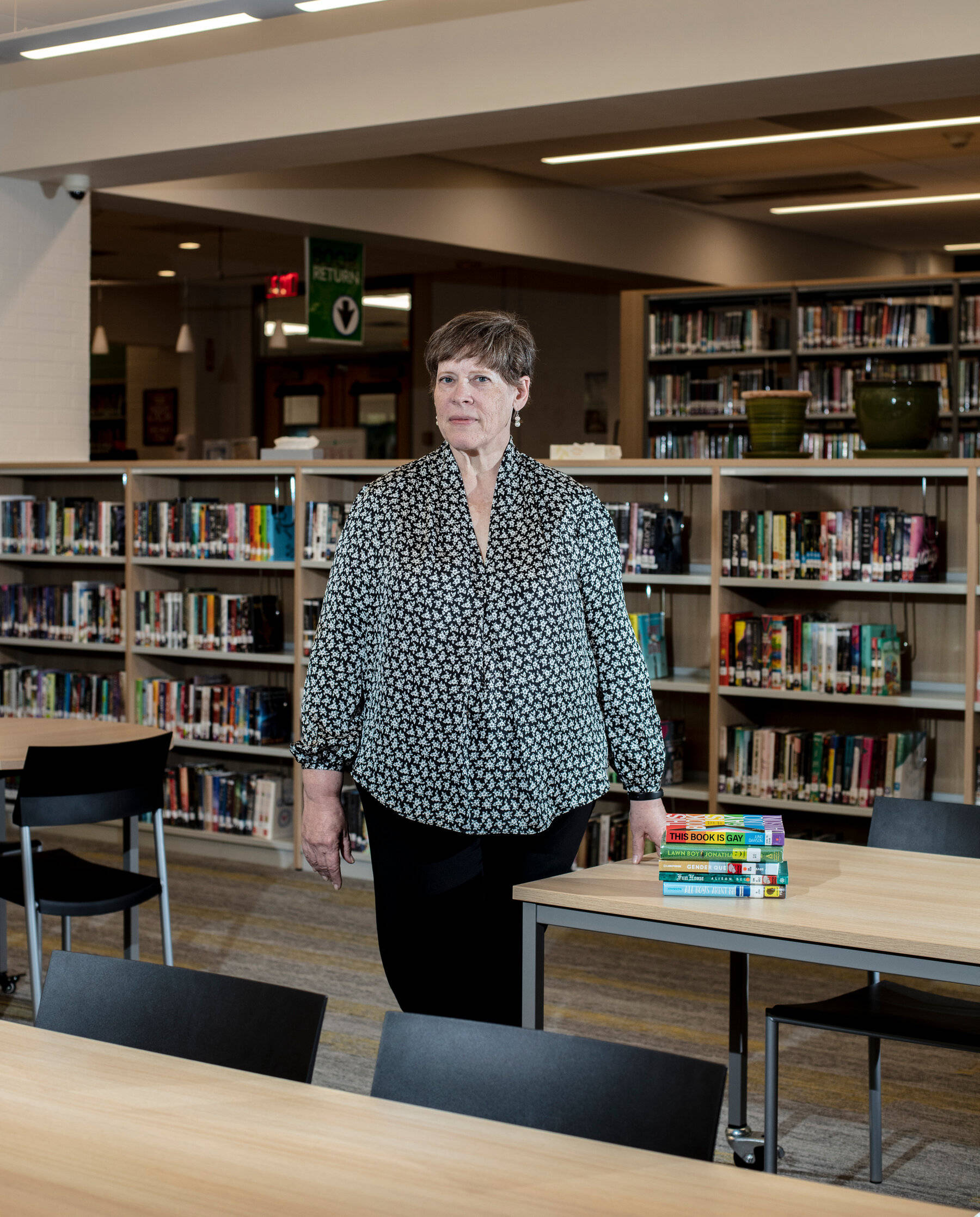Library 桌布 壁紙 — 一位身穿圖案襯衫的女性站在現代圖書館中，周圍是書架和學習桌。