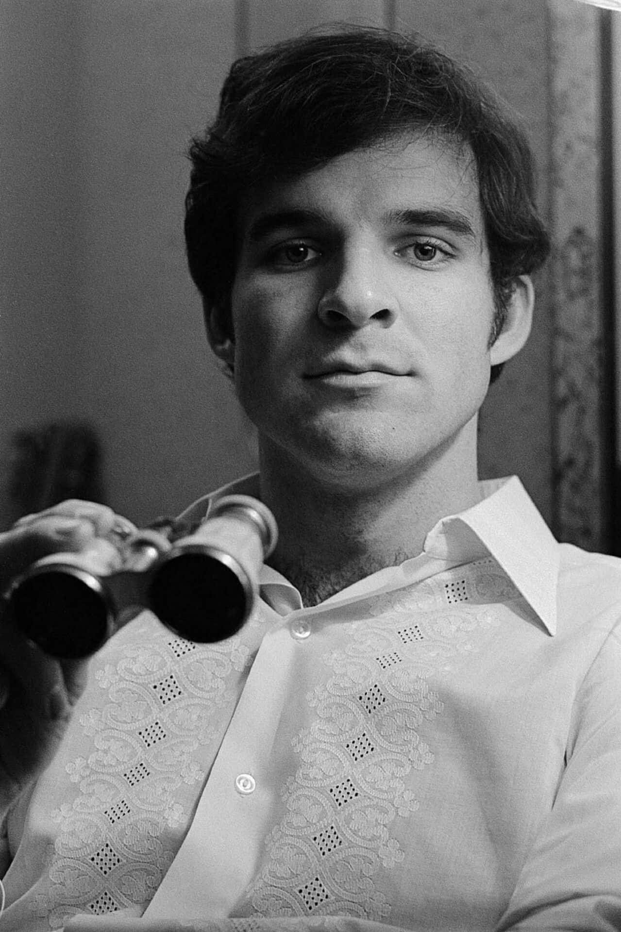 steve martin 桌布 壁紙 — 一位身穿圖案襯衫的年輕男子手持雙筒望遠鏡，在黑白肖像中直視鏡頭。