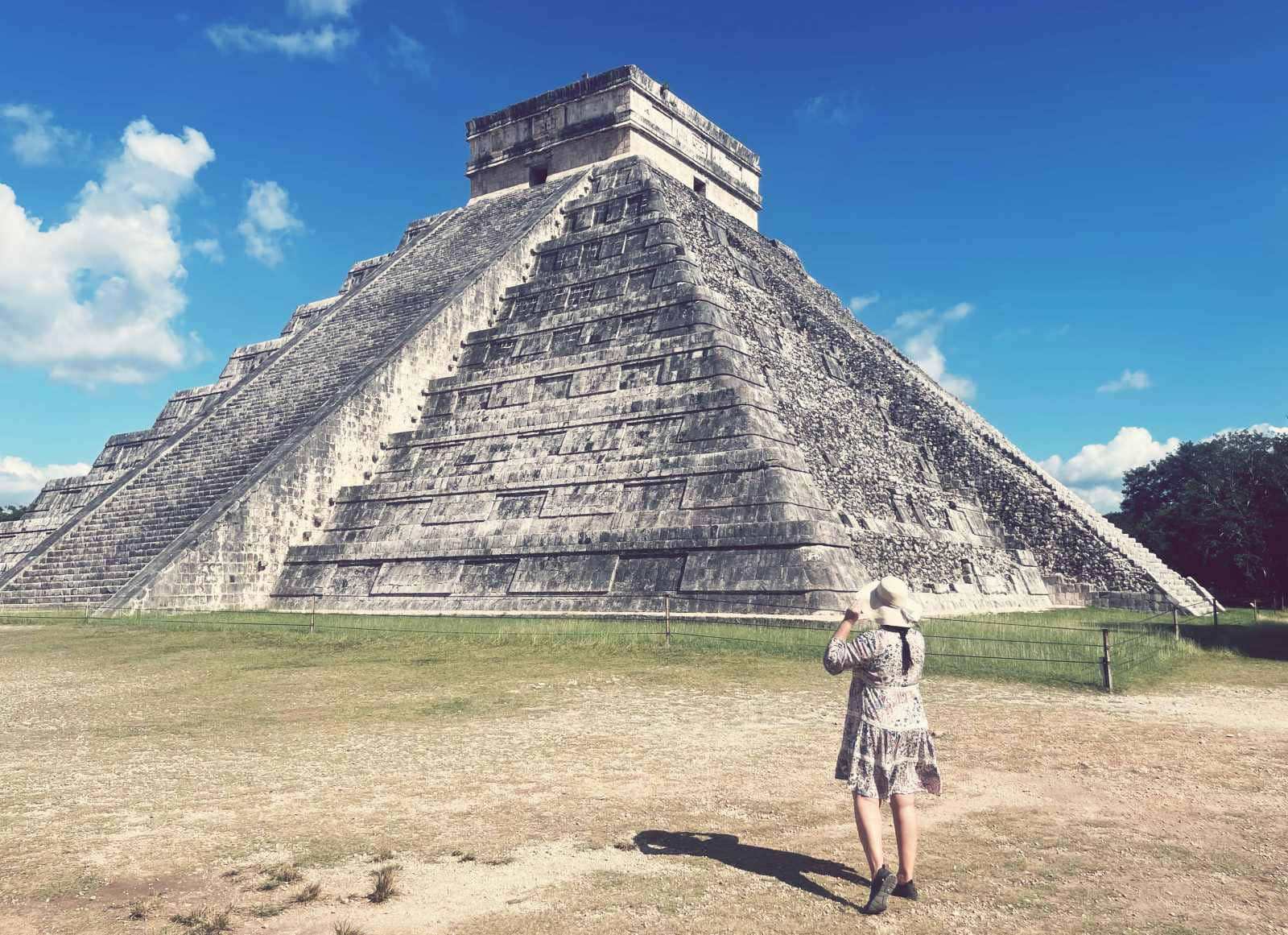Woman 桌布 壁紙 — 一位身穿圖案連衣裙和帽子的孤獨旅行者，站在明亮的藍天和散雲下，面對著巨大的奇琴伊察古瑪雅金字塔。