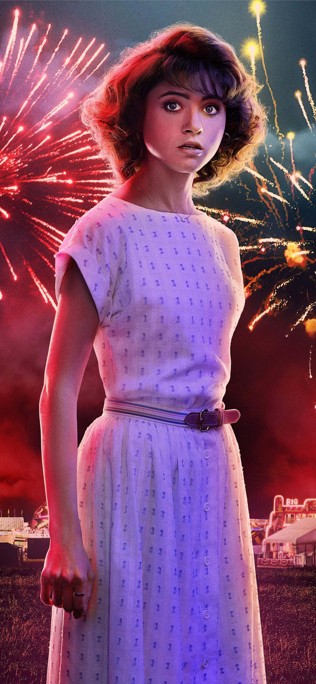Stranger Things Girly 桌布 壁紙 — 一位身穿圖案連衣裙的年輕女子，帶著驚訝的表情站在耀眼的煙火下。