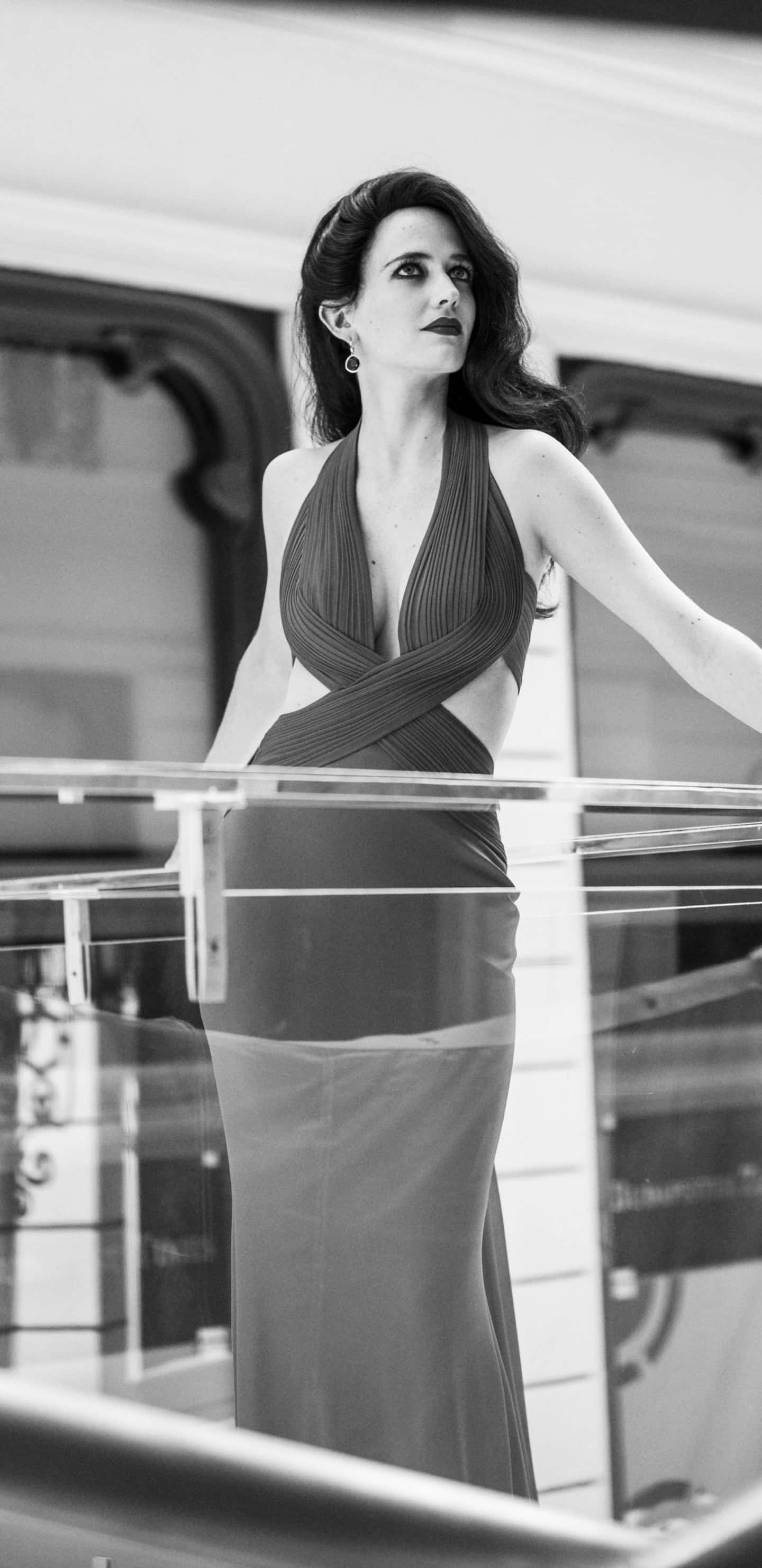 eva green 桌布 壁紙 — 一位身穿垂墜長袍的優雅女士，在單色肖像中優雅地站在玻璃陽台上。